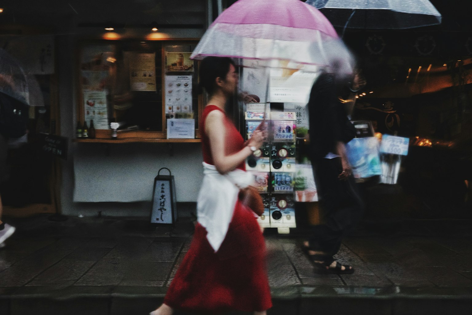 ผู้หญิงในชุดแดงเดินถือร่มสีชมพูในถนนเมือง