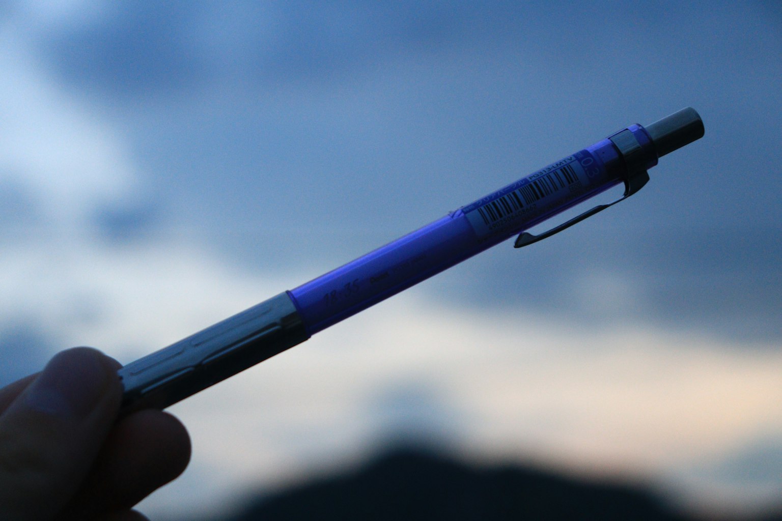 Un stylo à bille bleu-violet tenu contre un ciel crépusculaire