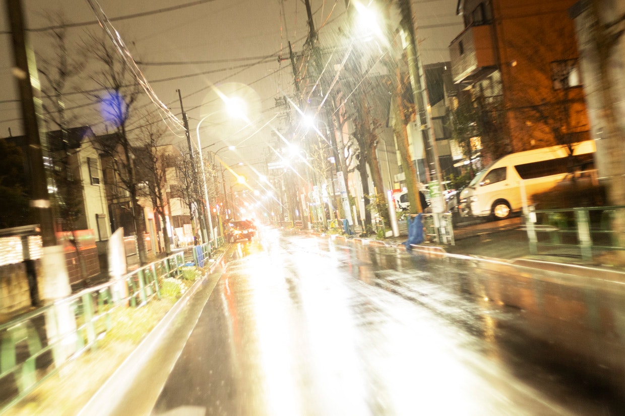 夜の街路で光がにじむ車道と街灯の並ぶ風景