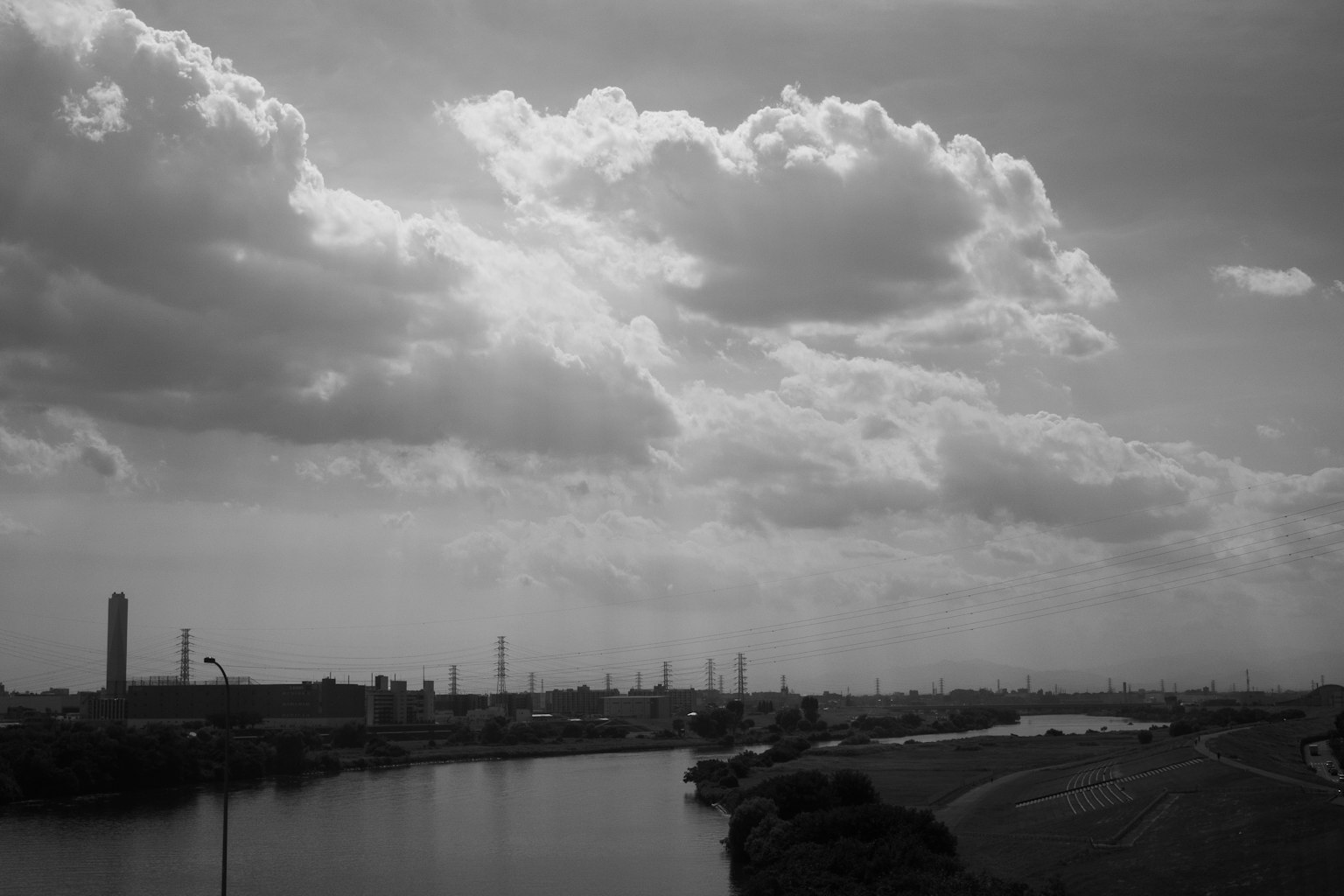 Black and white landscape photo showing an industrial area and a river large clouds fill the sky