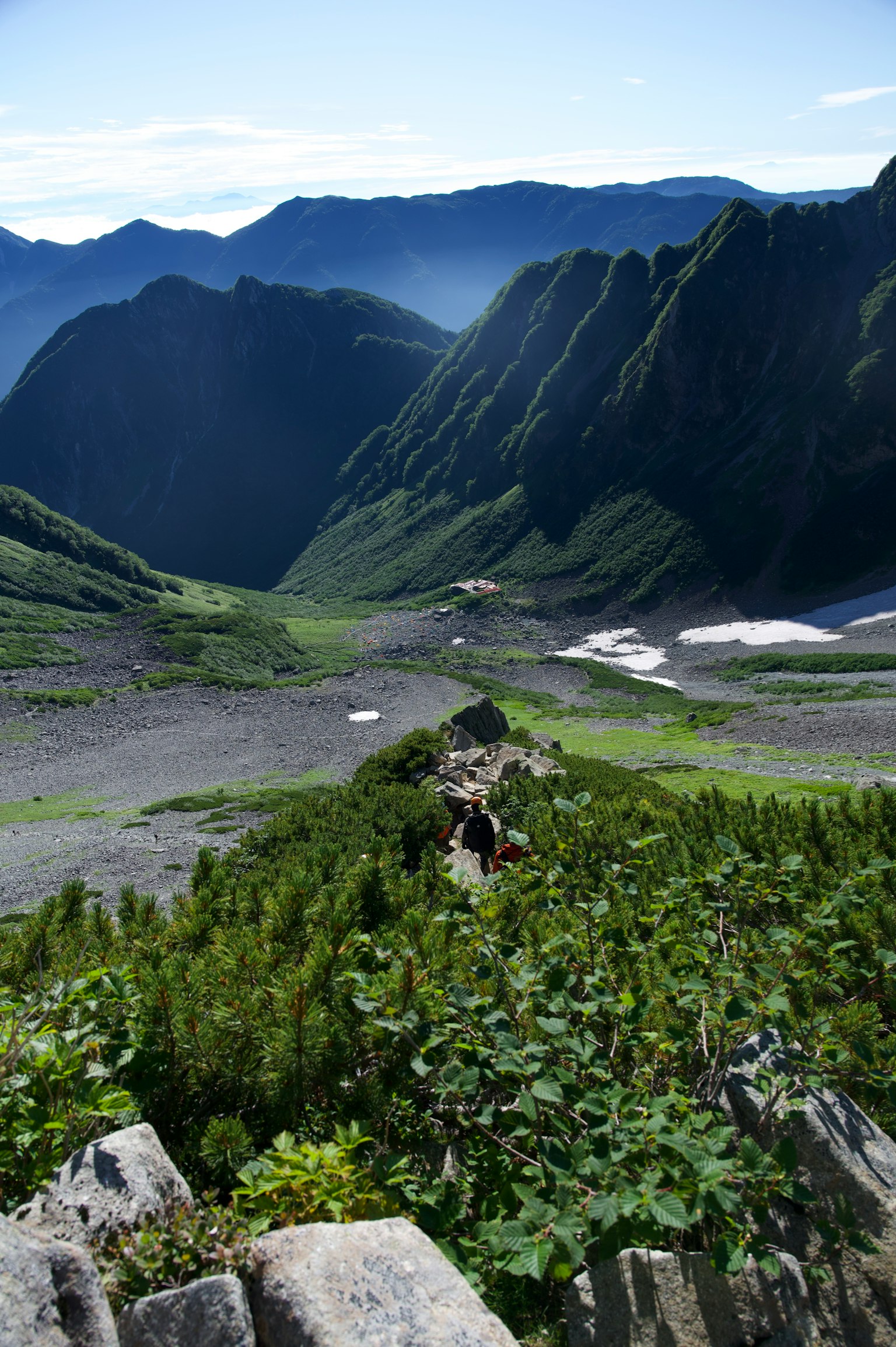 Vista escénica de un valle rodeado de montañas con vegetación verde y caminos rocosos