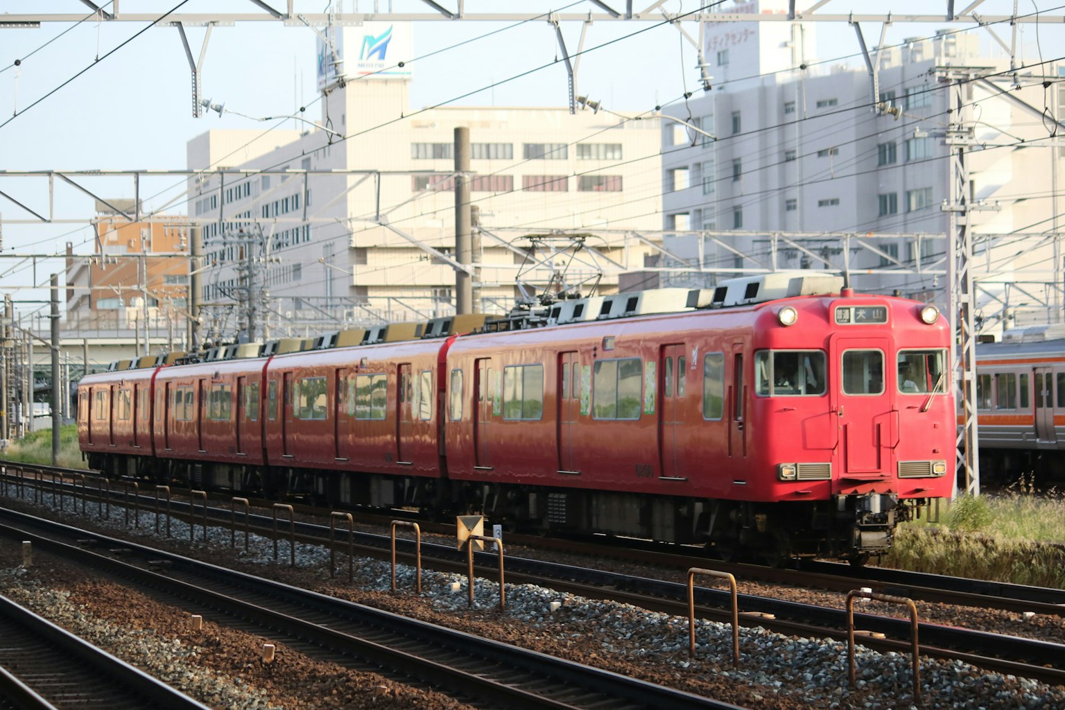 一列紅色火車在軌道上行駛，背景有建築物