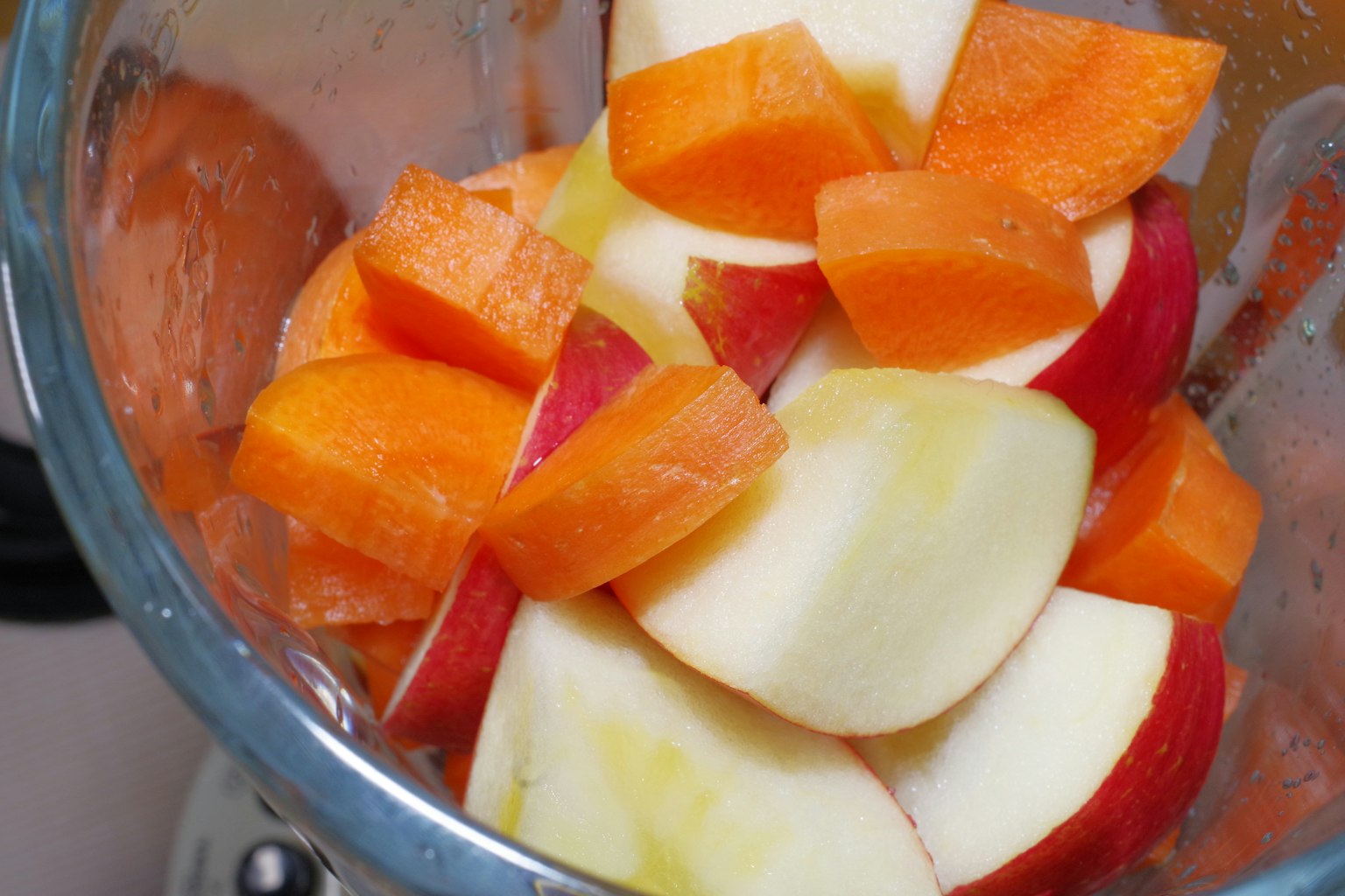 Pommes rouges et carottes oranges hachées dans un mixeur
