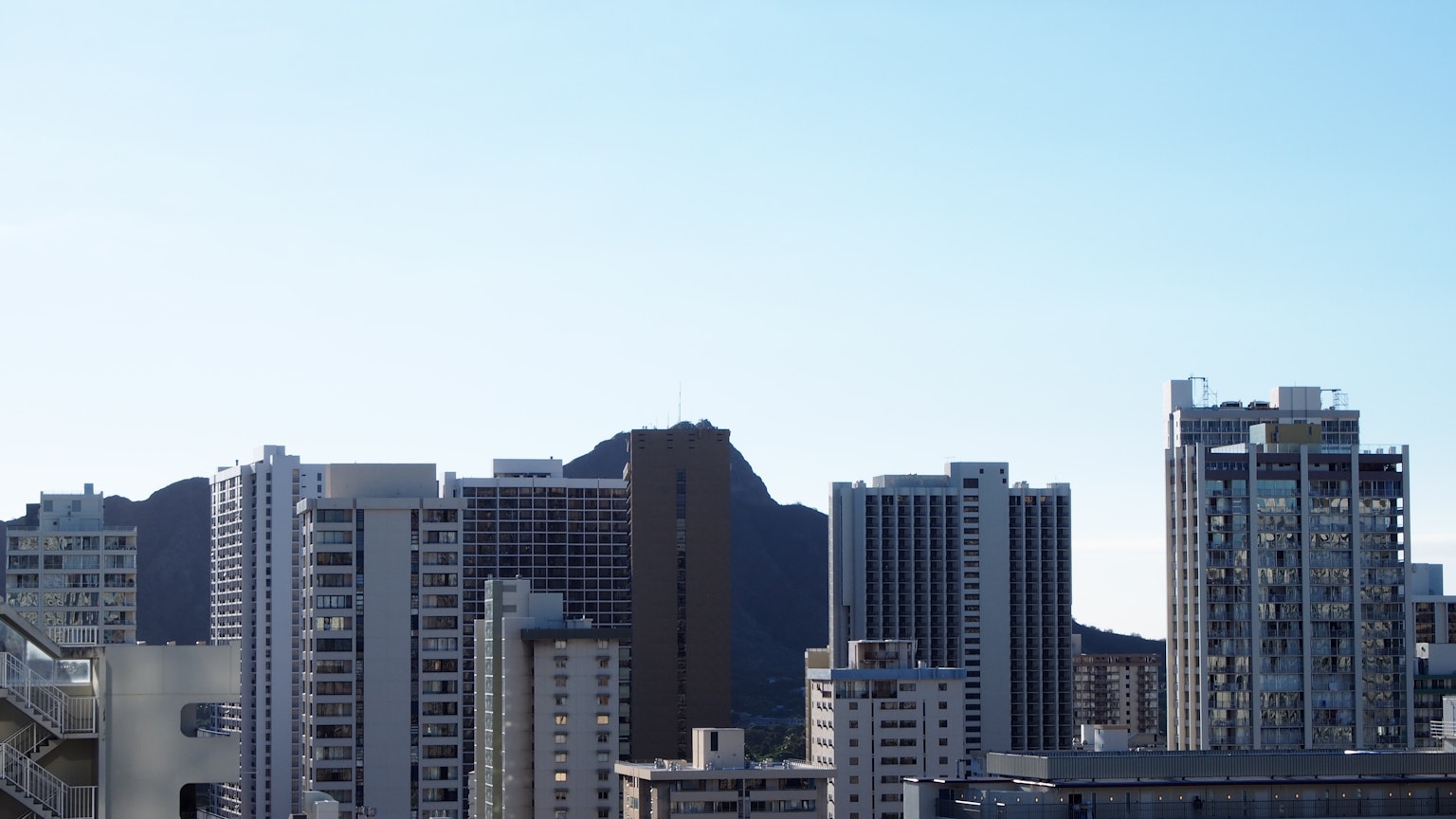 เส้นขอบฟ้าของเมืองที่มีตึกสูงและ Diamond Head ใต้ท้องฟ้าสีฟ้าใส