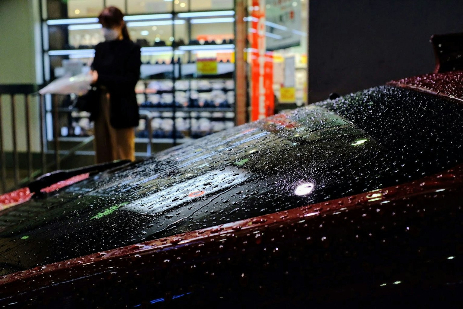 Cofano di auto rossa coperto di gocce di pioggia con una persona sullo sfondo