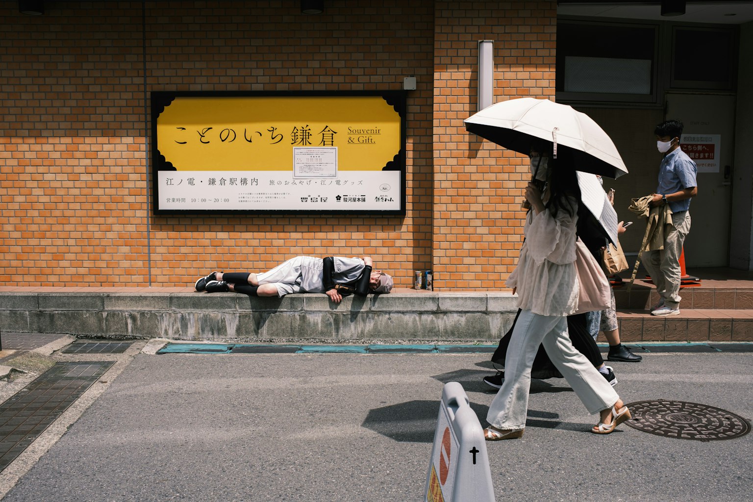 A man lying on the sidewalk with a woman walking by holding an umbrella