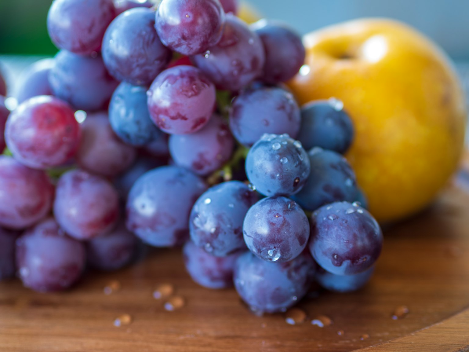 Purple grapes and a yellow apple arranged on a wooden board