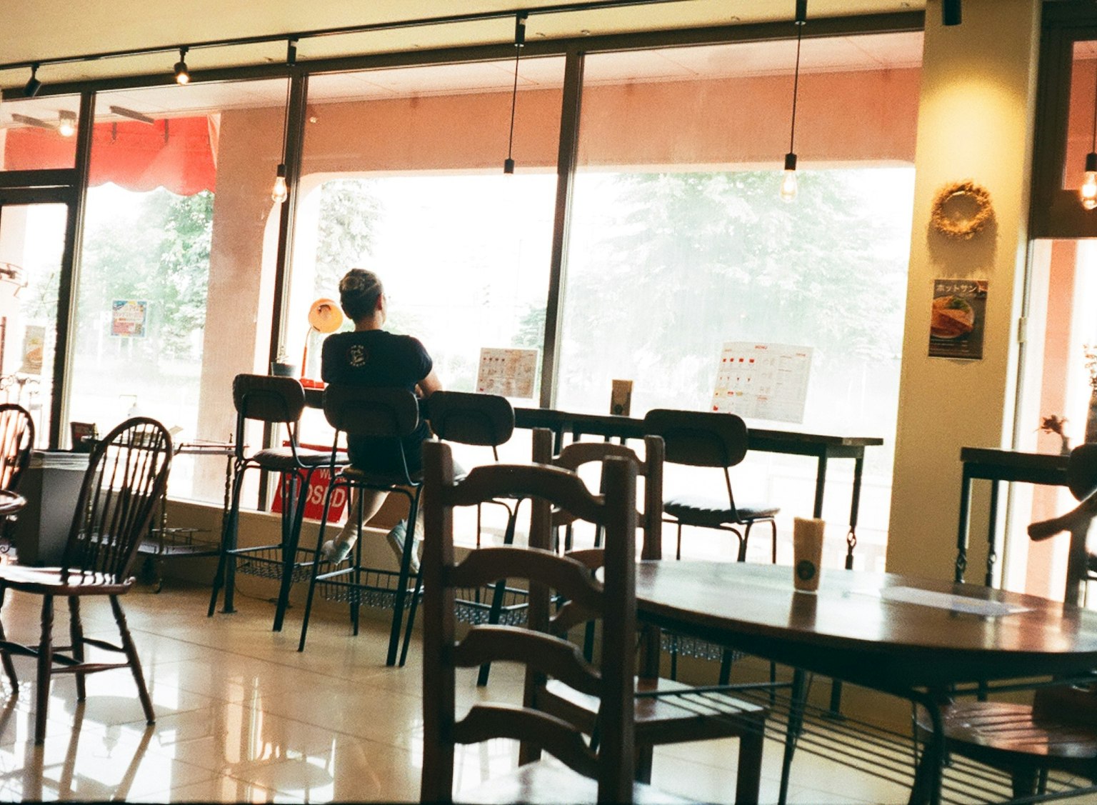 Interno di un caffè con una persona seduta vicino alla finestra e tavoli