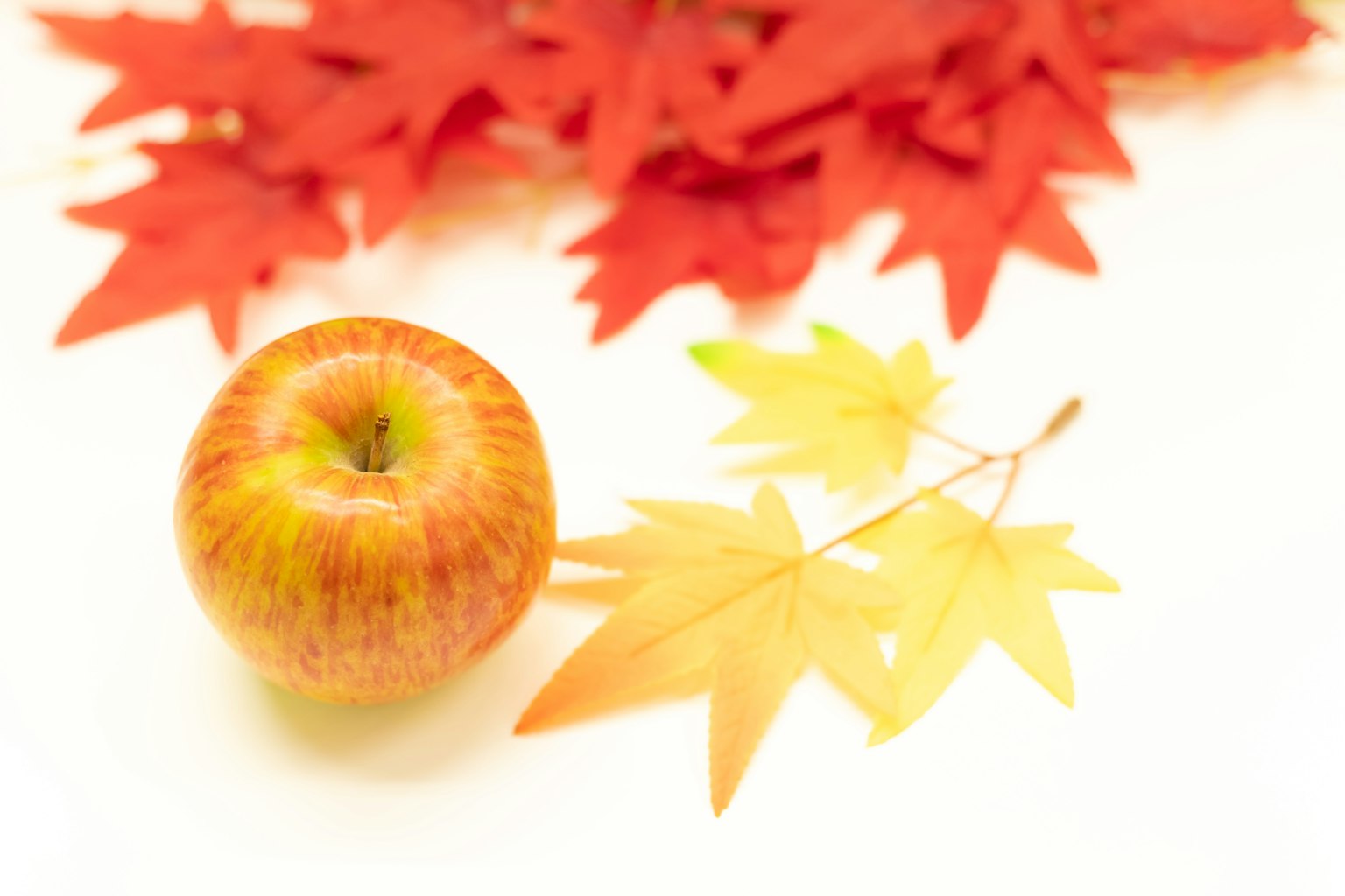 Une pomme placée parmi des feuilles d'automne rouges et jaunes