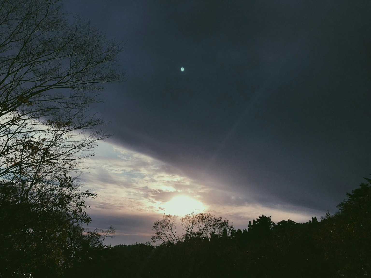 Un paesaggio con un piccolo sole visibile tra nuvole scure