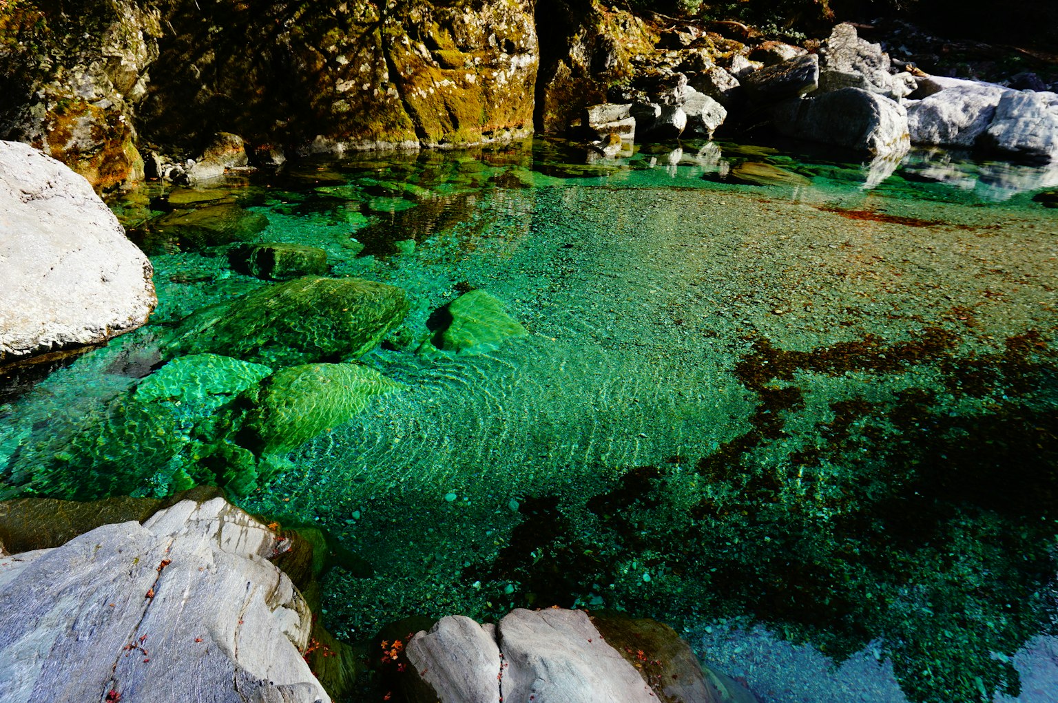 清澈的碧綠水流過岩石河床，綠色石頭點綴其間