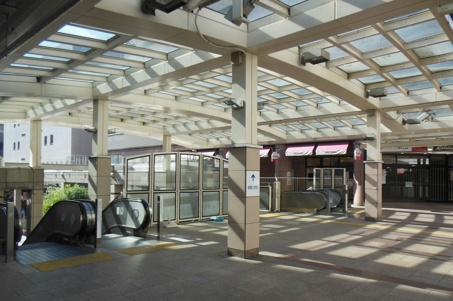 Área de estación interior brillante con escaleras mecánicas y techo transparente