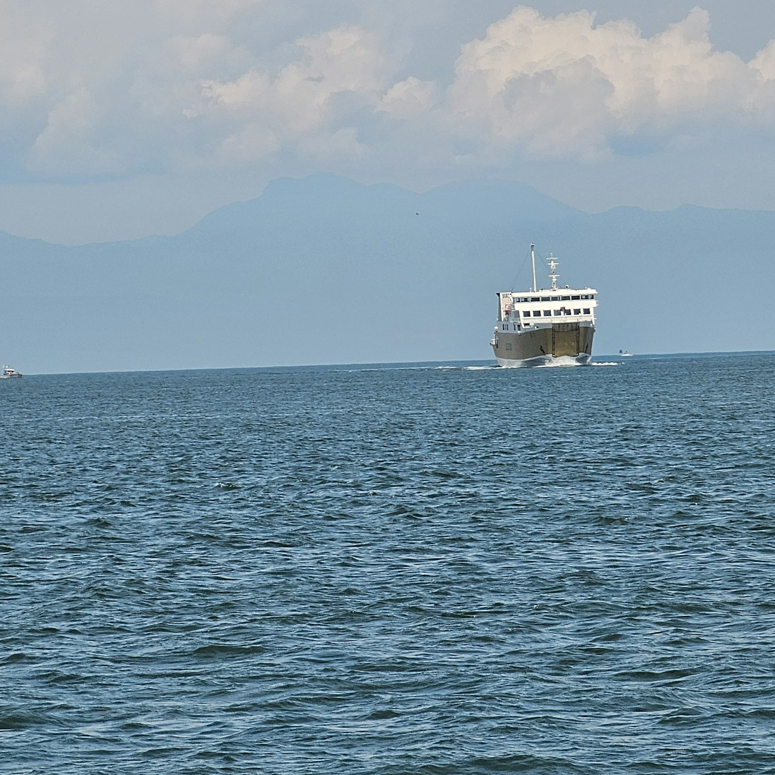 Sebuah kapal berlayar di laut biru dengan gunung di latar belakang