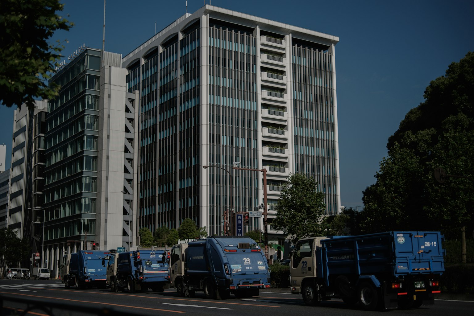 Rangée de camions à ordures bleus devant un immeuble de bureaux moderne