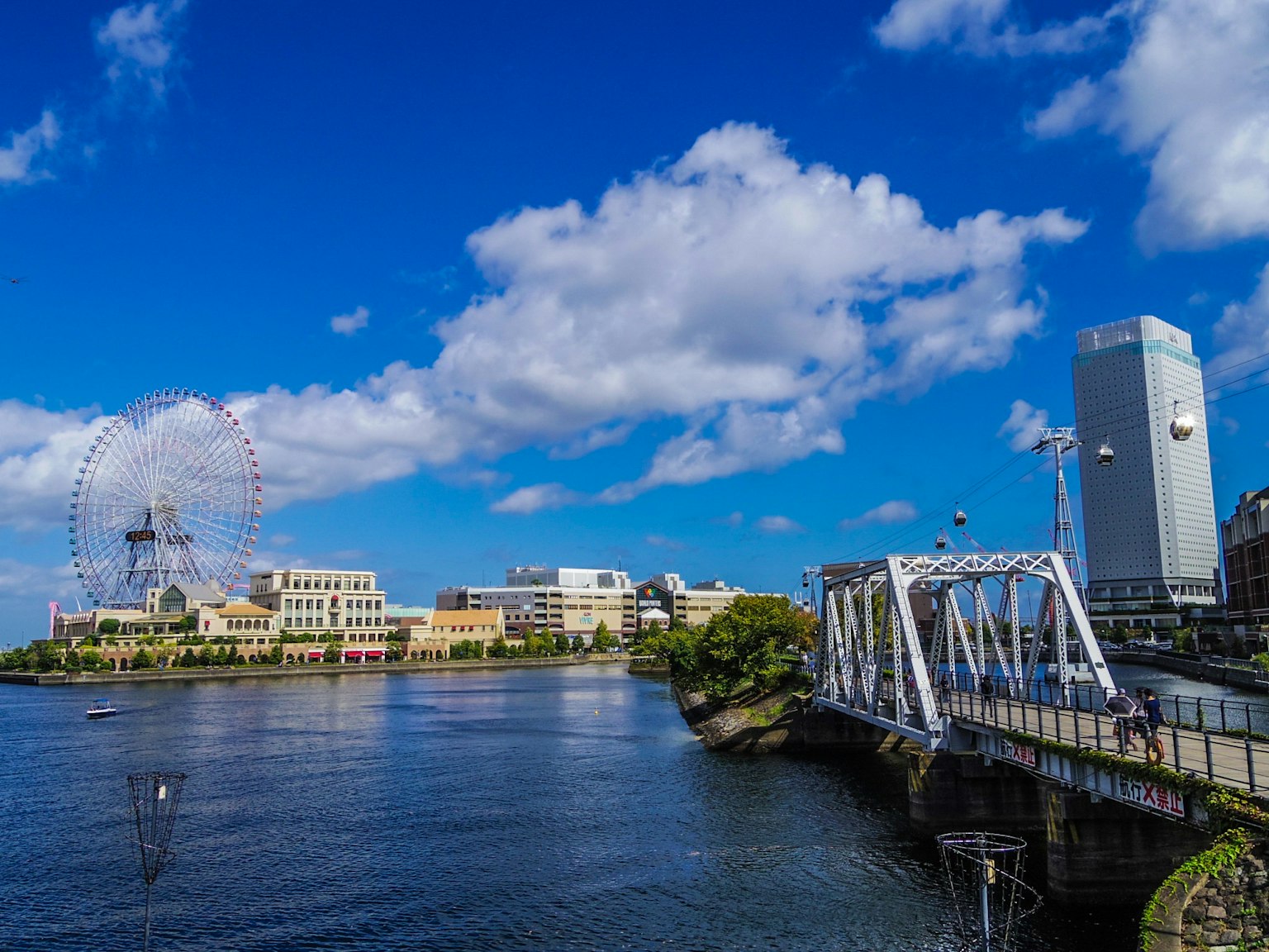 Vista panoramica di un fiume con un ponte sotto un cielo blu e nuvole bianche con vari edifici e una ruota panoramica