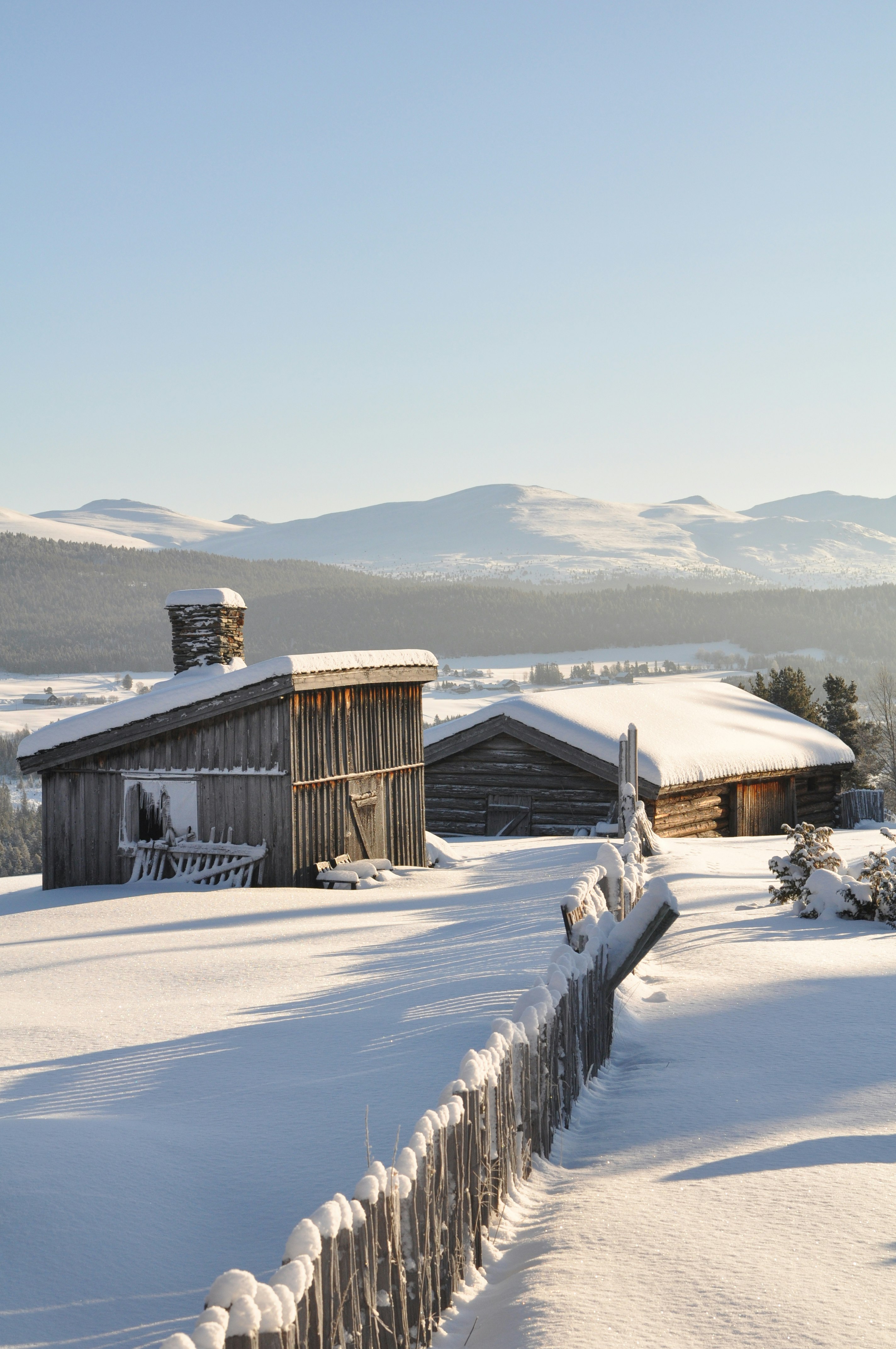 雪に覆われた山あいの木造小屋と柵のある風景