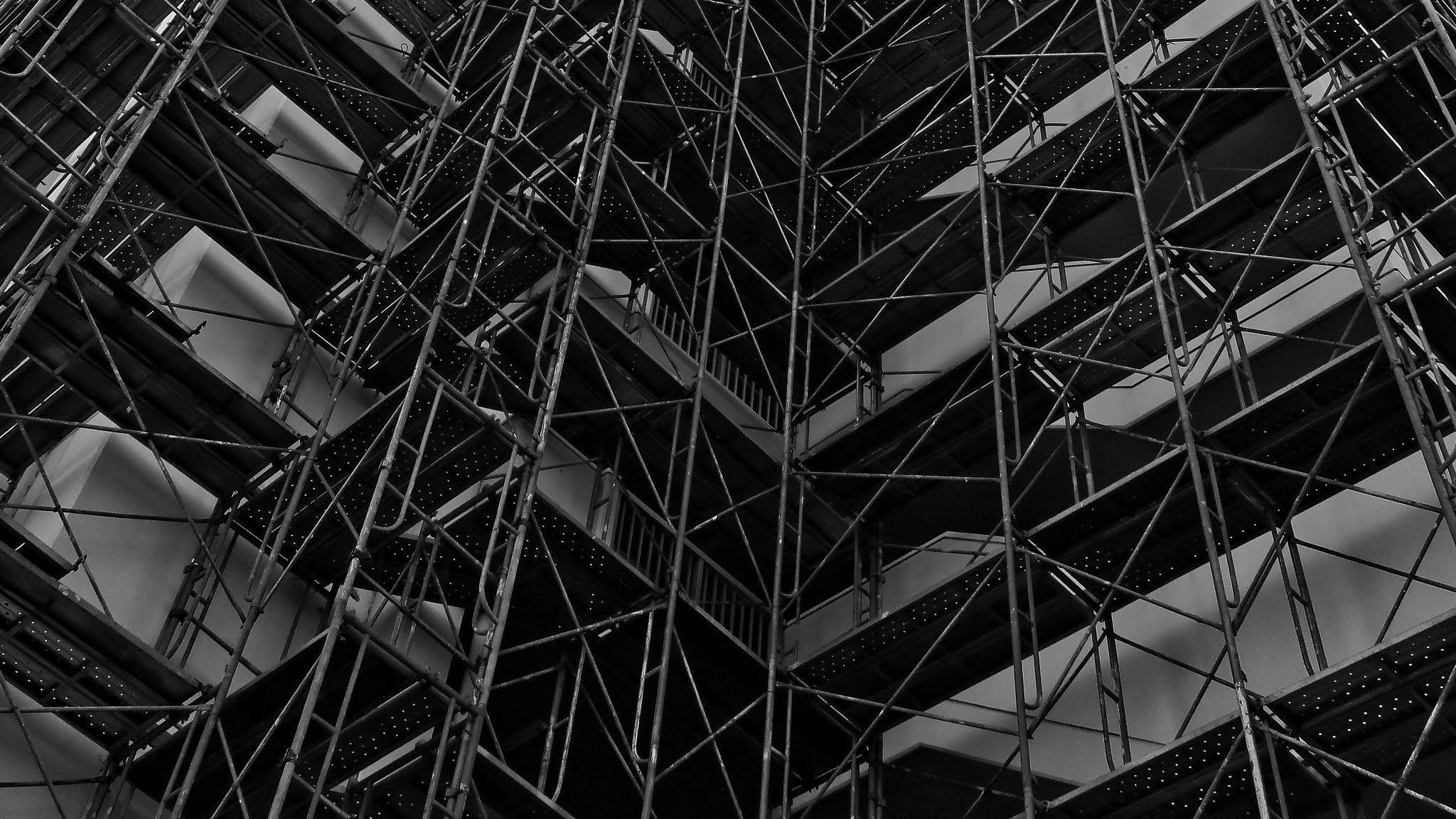 外壁工事の足場を見上げるモノクロの建物内部空間