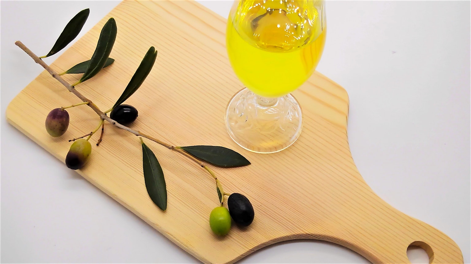 Gelbe Getränk in einem Glas auf einem Holzbrett mit Olivenzweig und Oliven