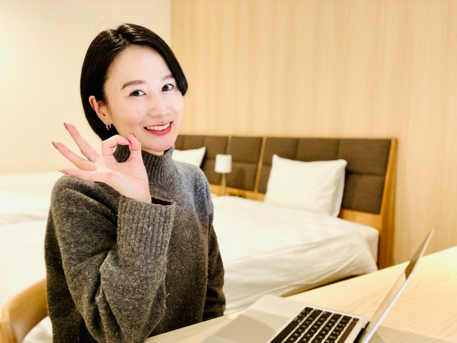 หญิงสาวยิ้มในเสื้อไหมพรมสีเทาทำท่าทาง OK ในห้องน่ารักพร้อมแล็ปท็อป