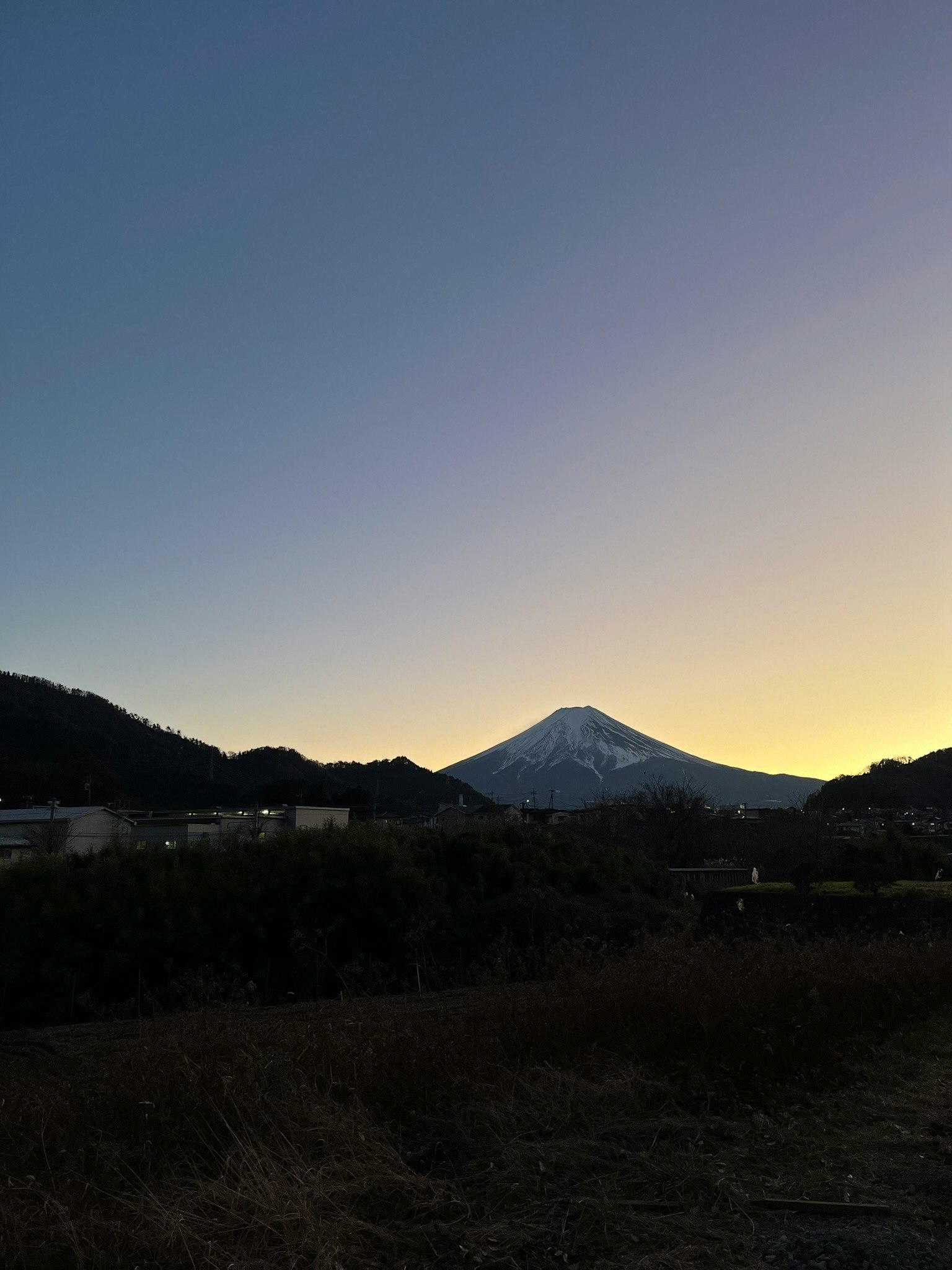 夕暮れの畑と山並み、遠くにそびえる火山のシルエット