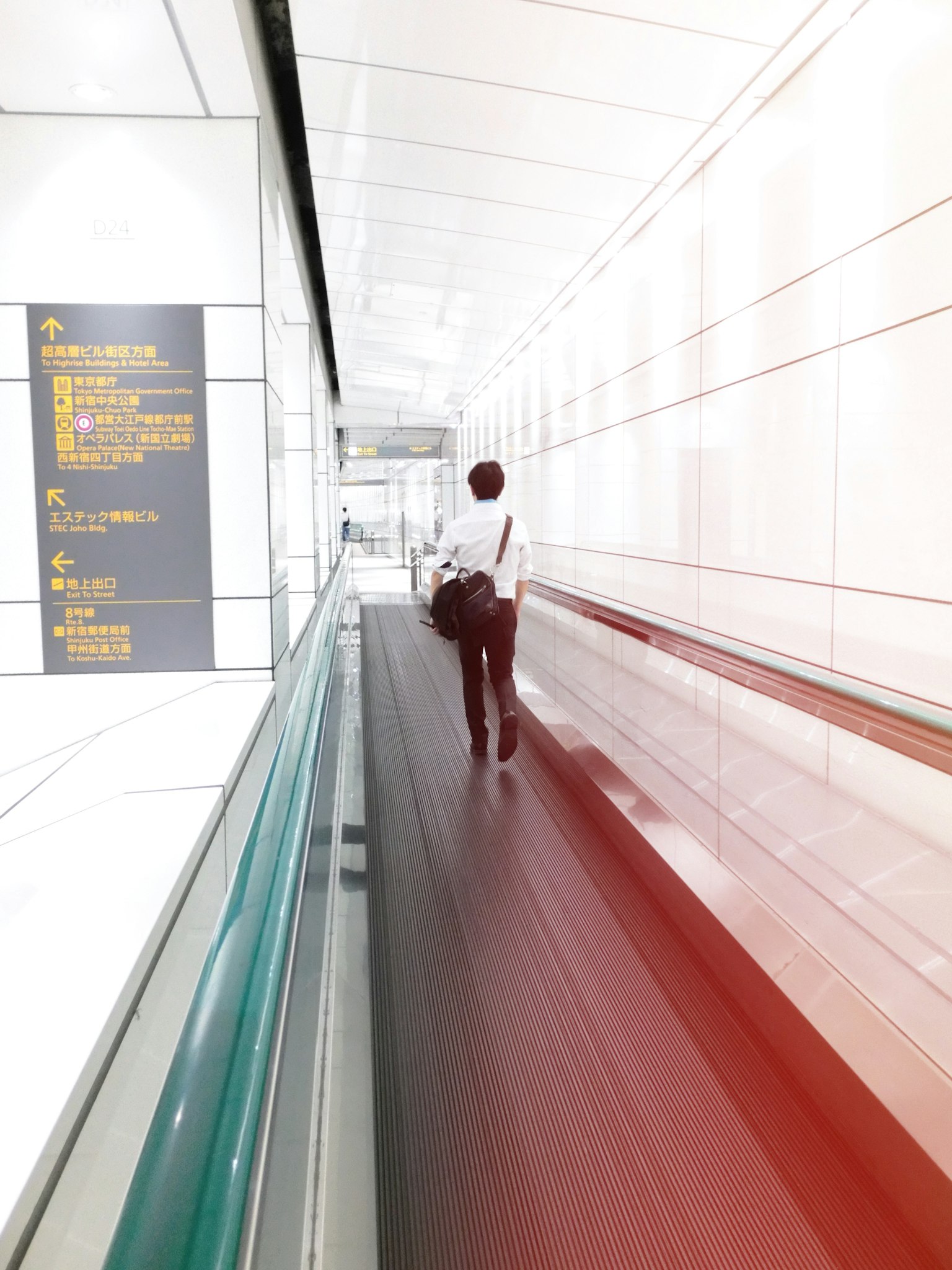 一个人在明亮的走廊中走，走廊有白色的墙壁和移动人行道