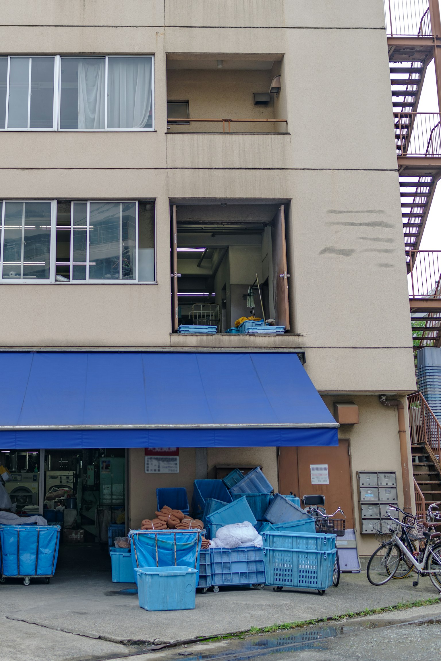 Exterior of a building with stacked blue baskets visible outside window and internal view from the second floor
