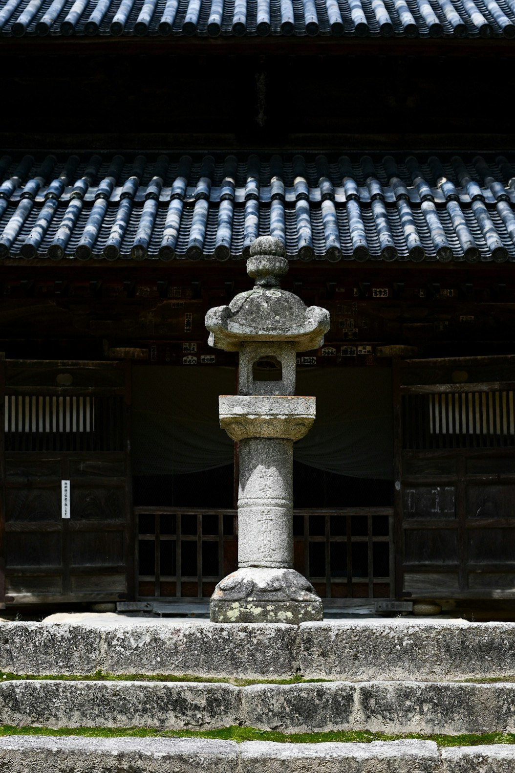 石造りの灯籠と瓦屋根のある寺院の門前