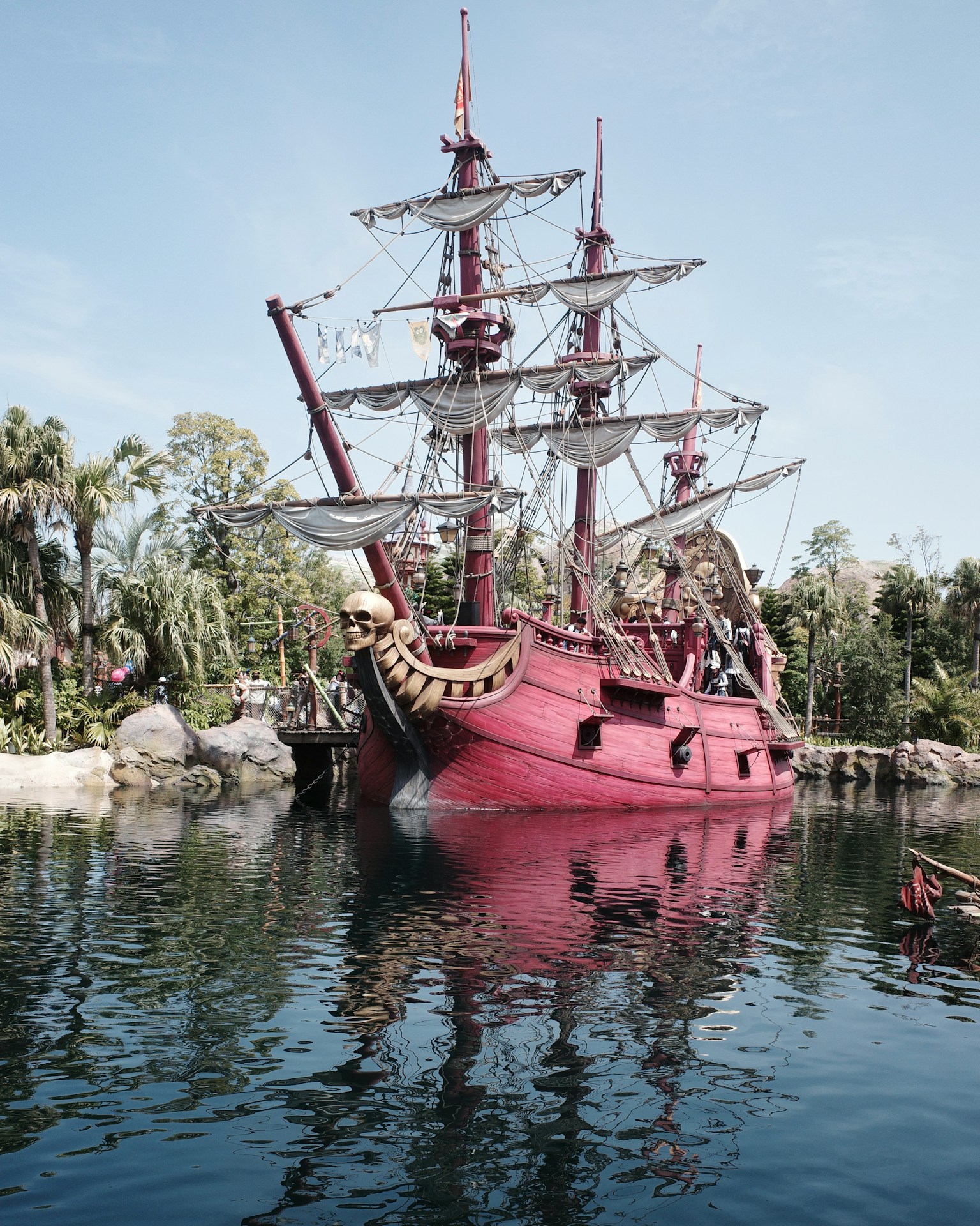 Una nave pirata rossa ormeggiata in un contesto verdeggiante riflessa nell'acqua
