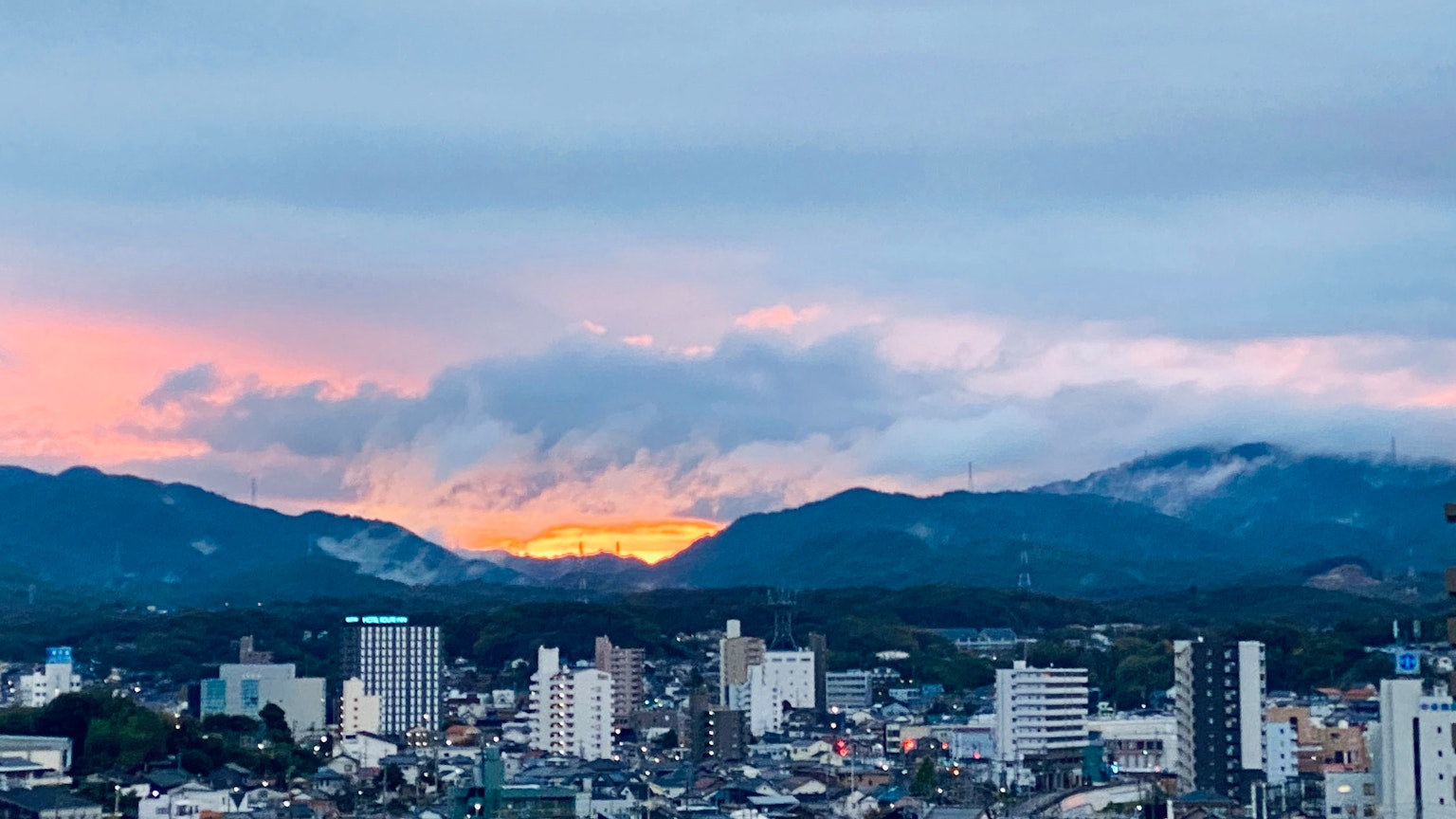 Pemandangan panorama kota dengan pegunungan saat matahari terbenam