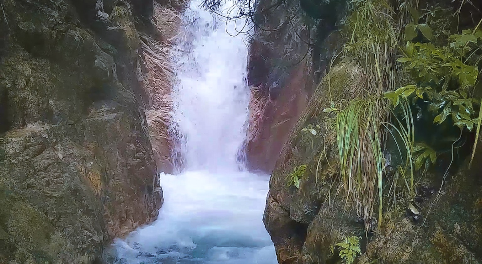 一幅風景如畫的瀑布在岩石懸崖之間流淌，周圍環繞著綠色植物