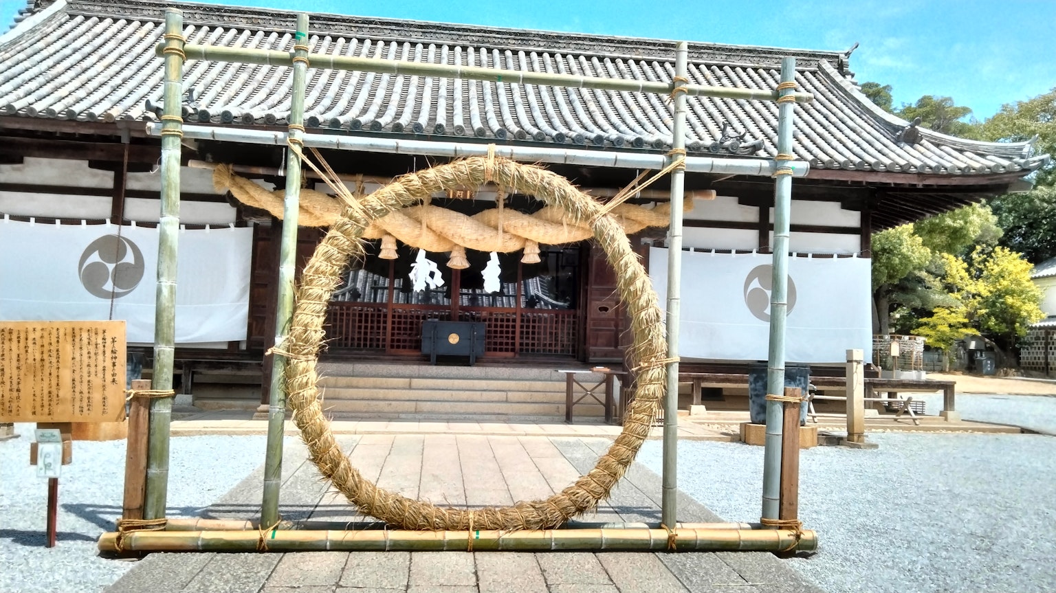 A large straw ring in front of a shrine with traditional architecture