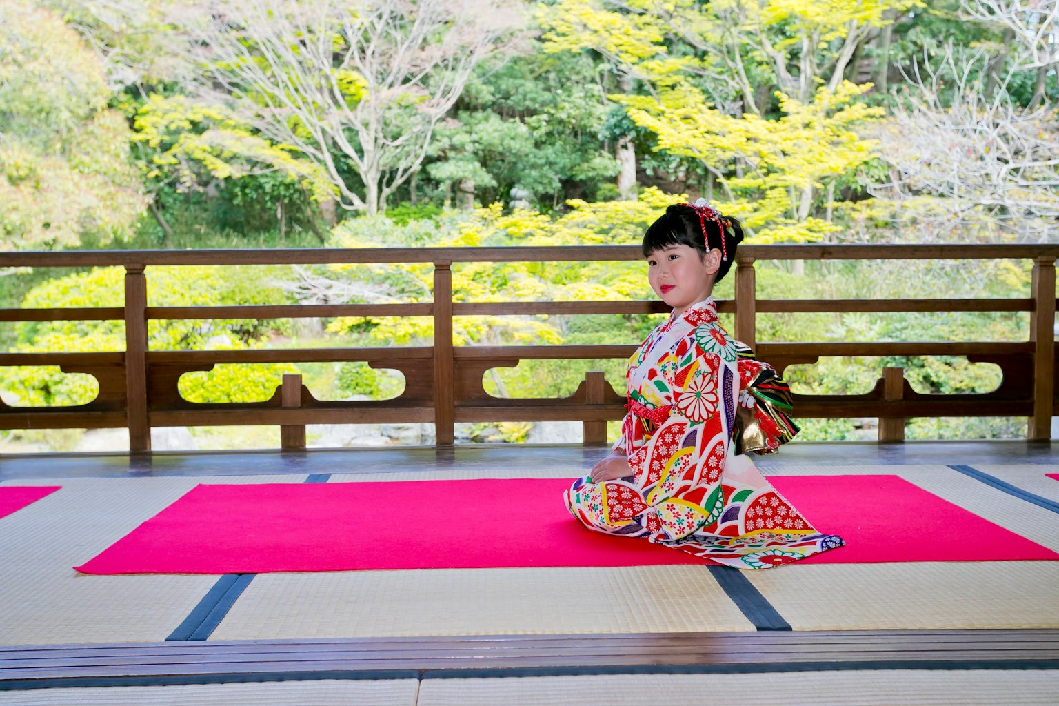 Una ragazza in kimono colorato seduta su un tappeto rosso