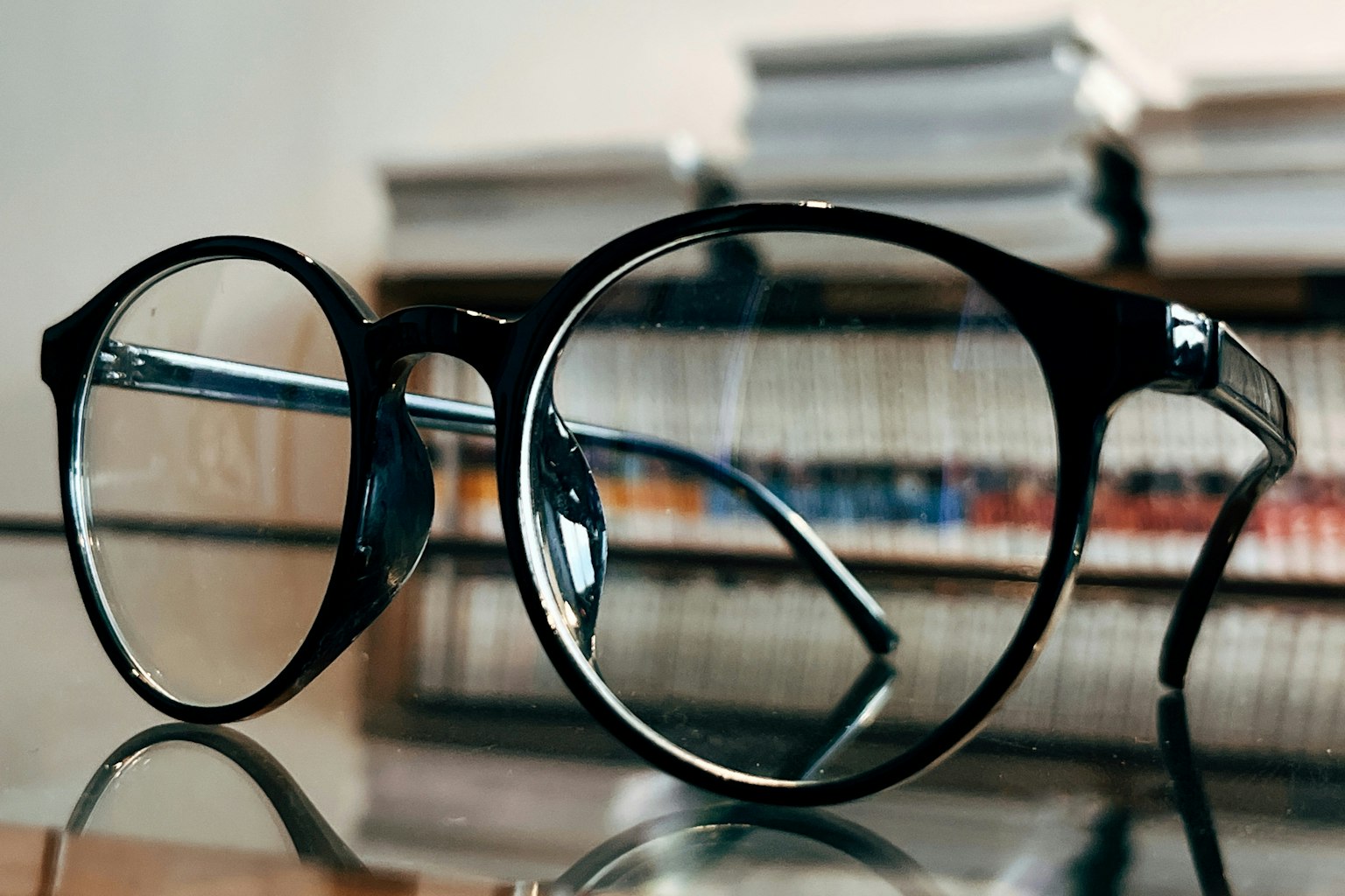 黒いフレームの眼鏡がテーブルの上に置かれている 背景には本が並んでいる