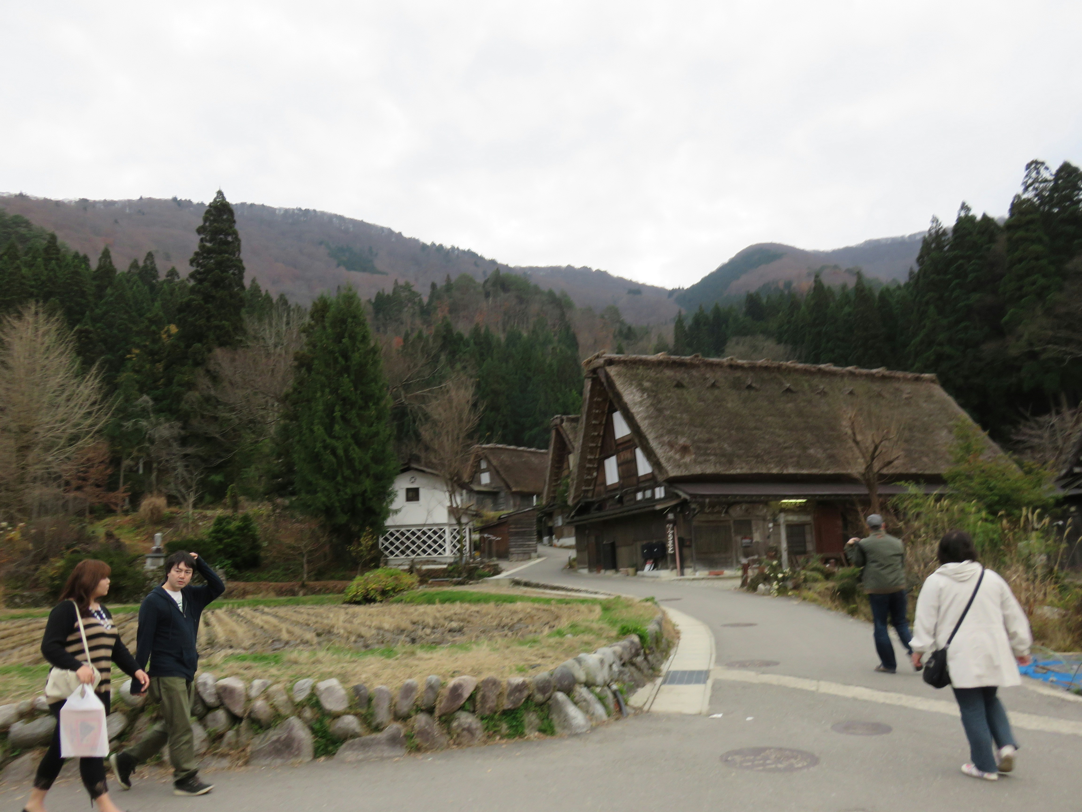 People walking along a path beside a traditional farmhouse in the mountains