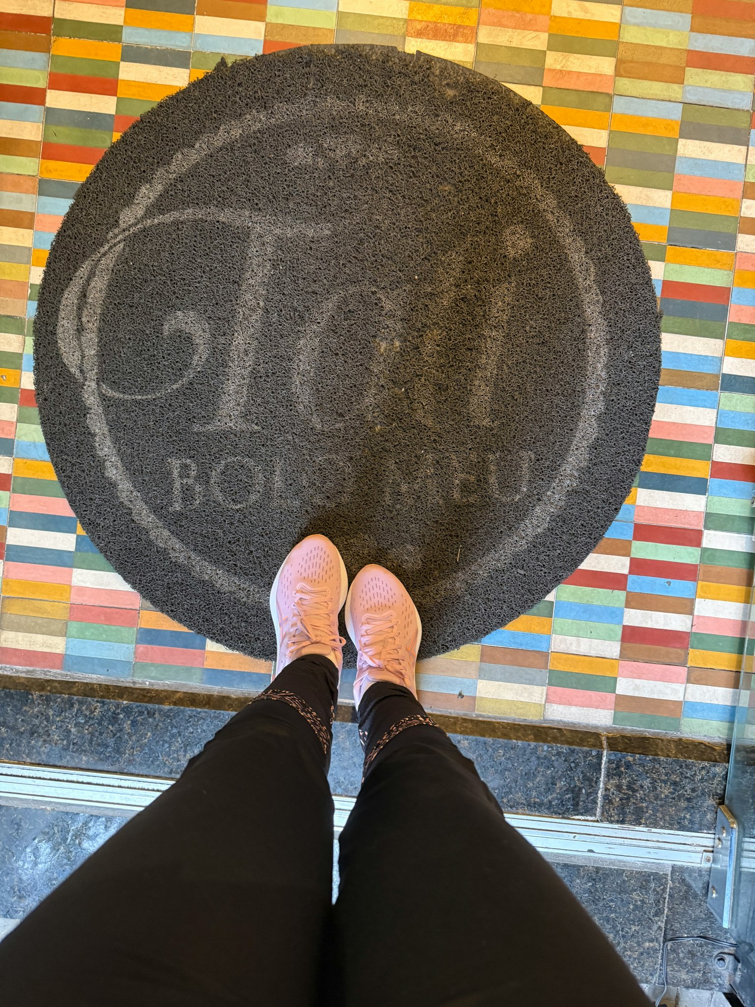 カラフルなタイルの上に立つピンクの靴とロゴ入りマット