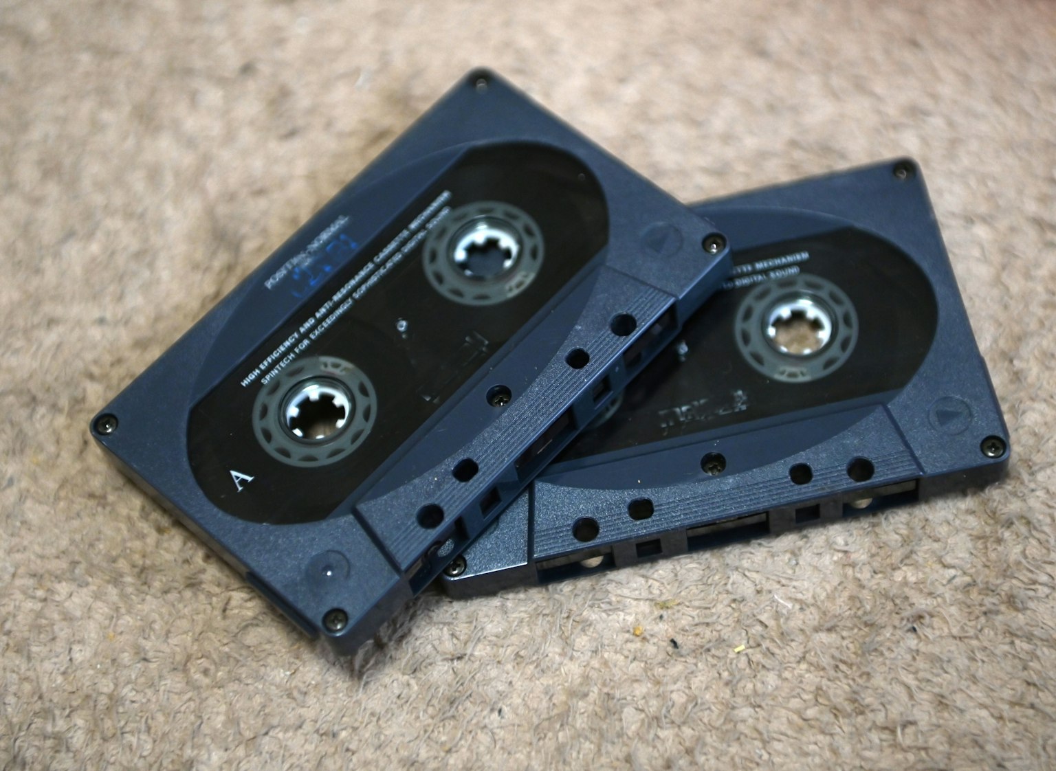 Two cassette tapes stacked on a carpeted surface