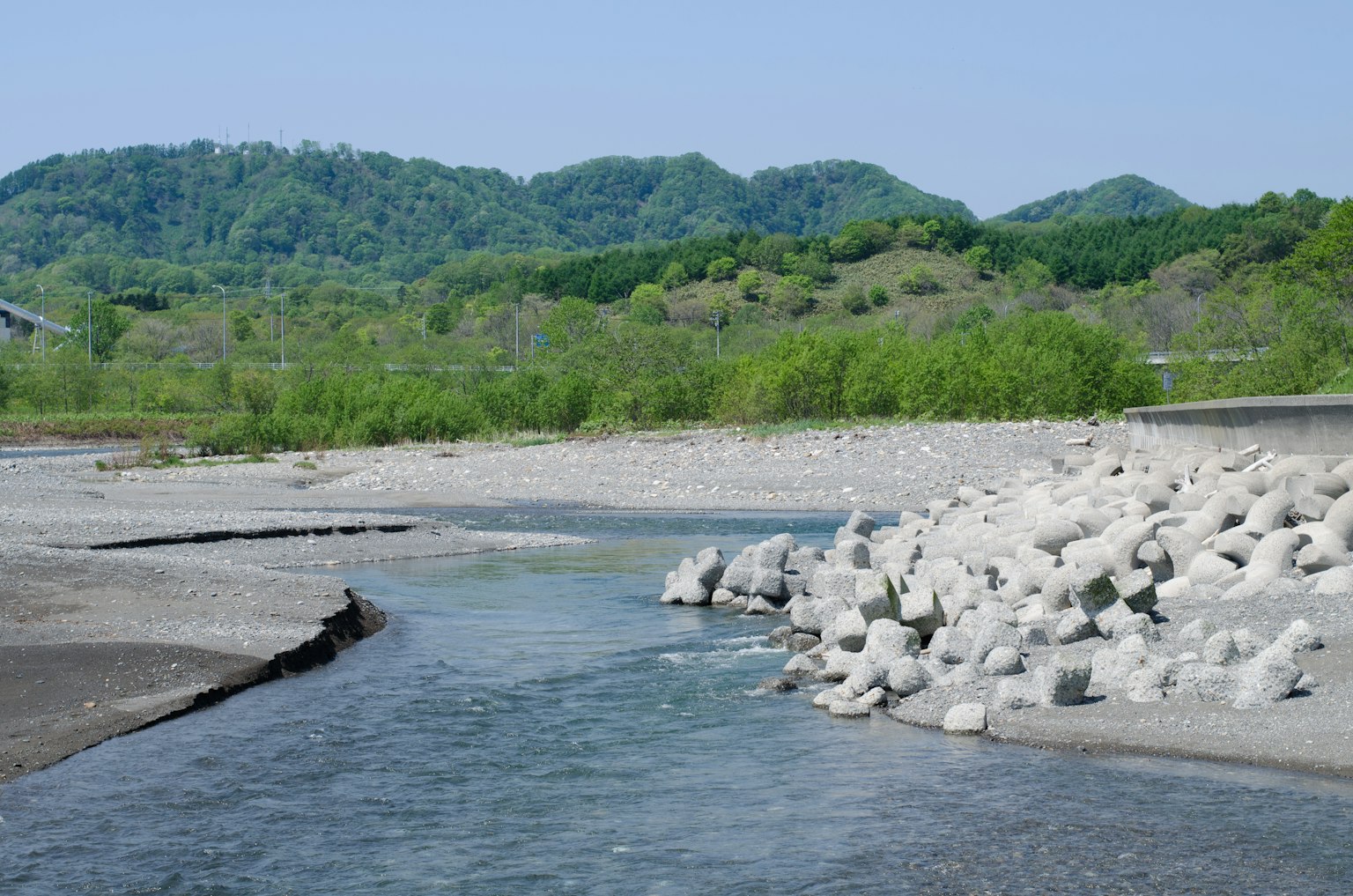 Malersicher Blick auf einen blauen Fluss mit grünen Hügeln im Hintergrund weiße Steine am Ufer