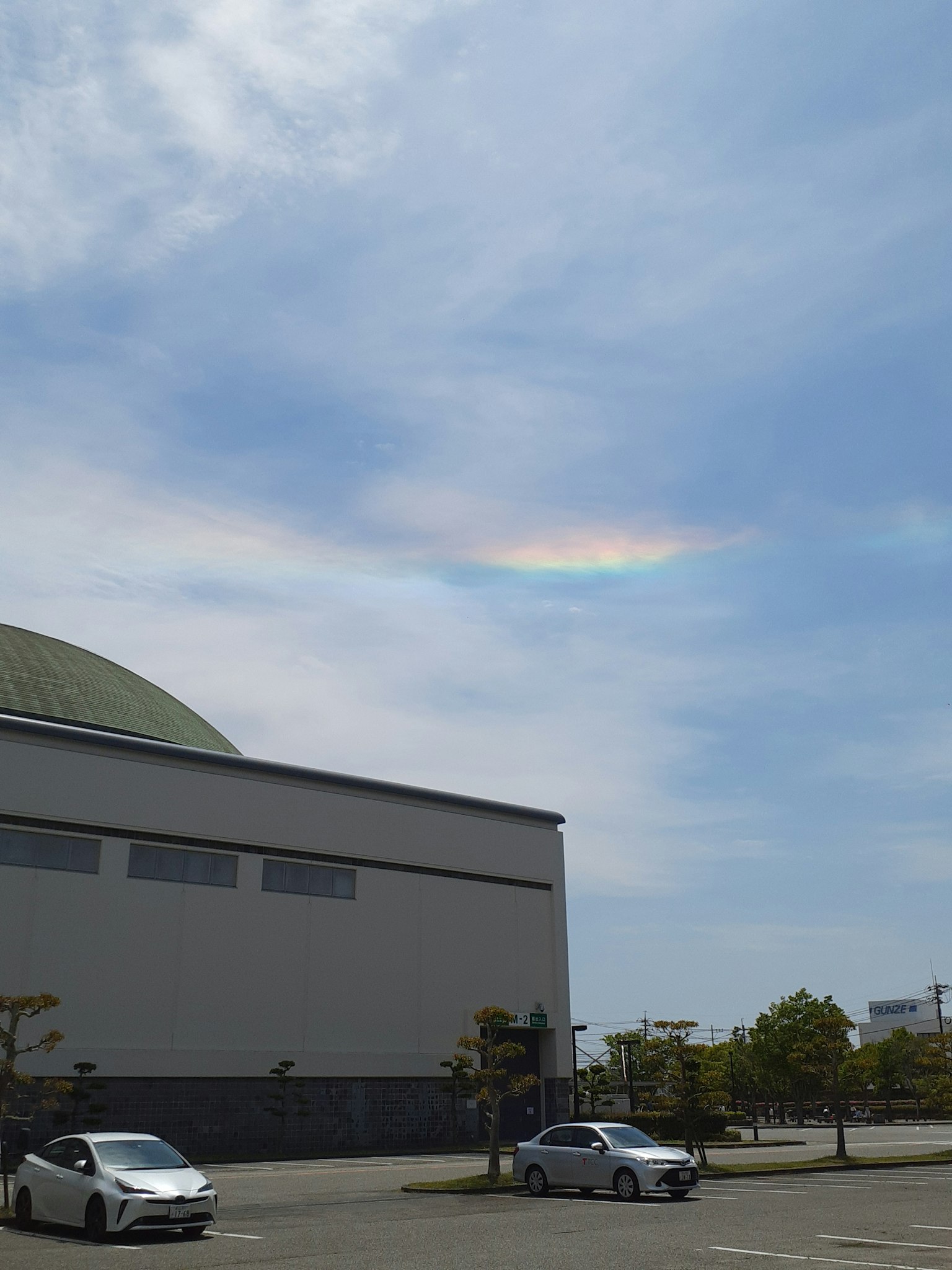 Una nuvola simile a un arcobaleno nel cielo blu con un edificio e auto parcheggiate