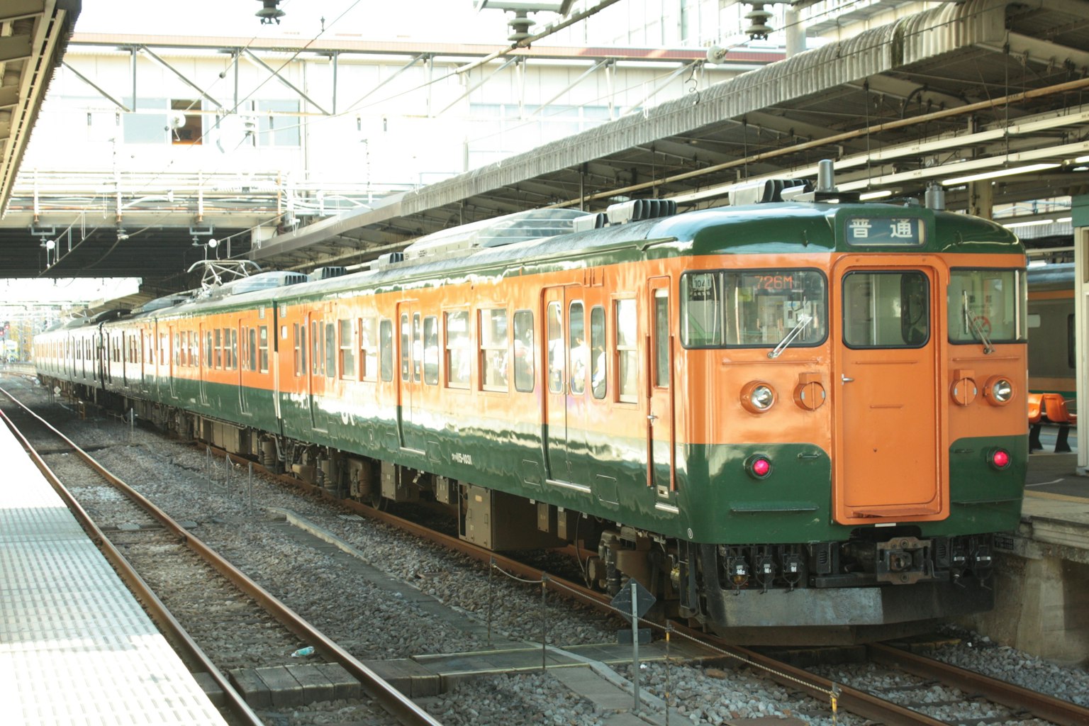 Sebuah kereta berwarna oranye dan hijau diparkir di stasiun