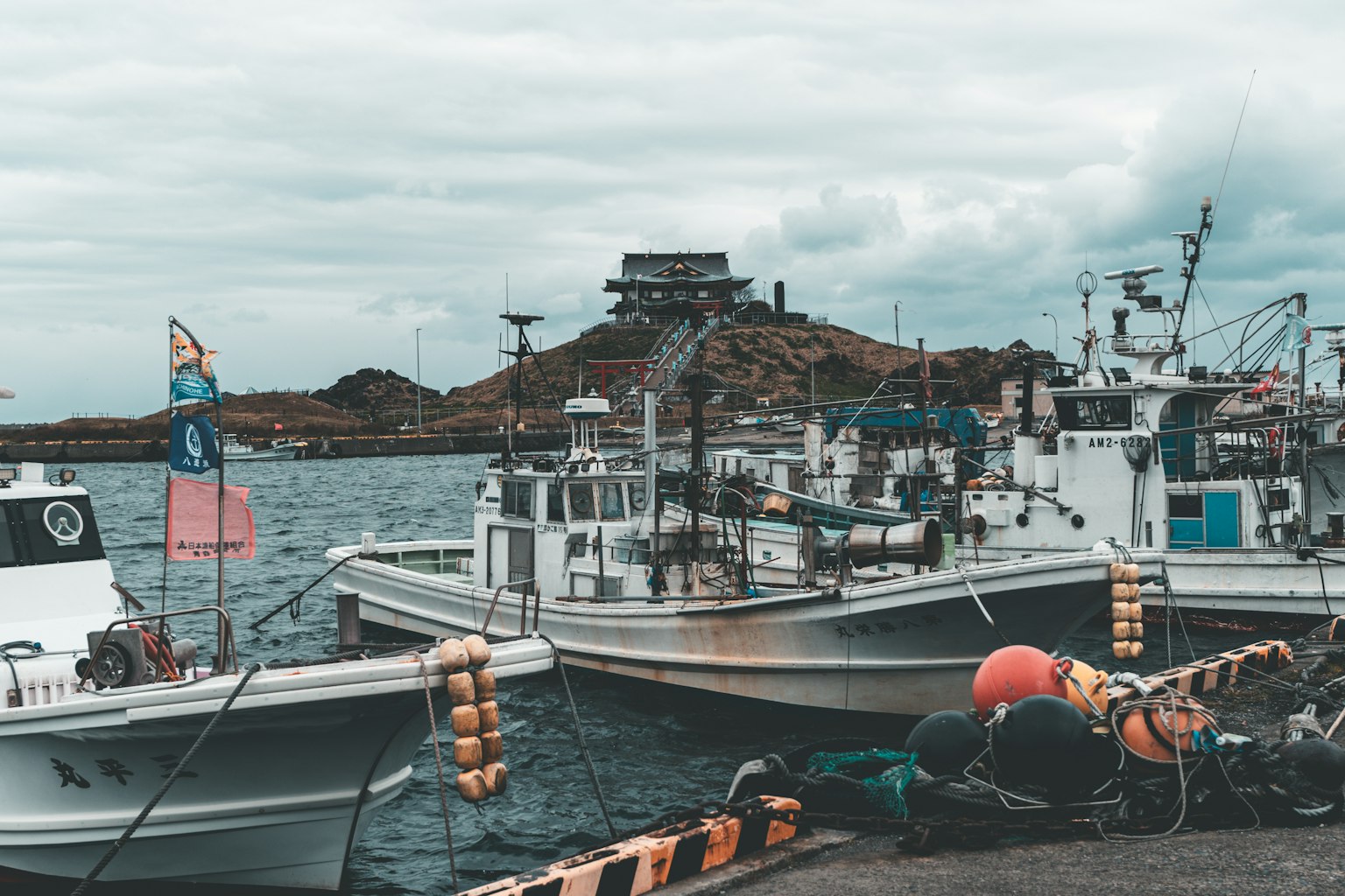 Fishing boats docked on the water with a building on a hill in the background