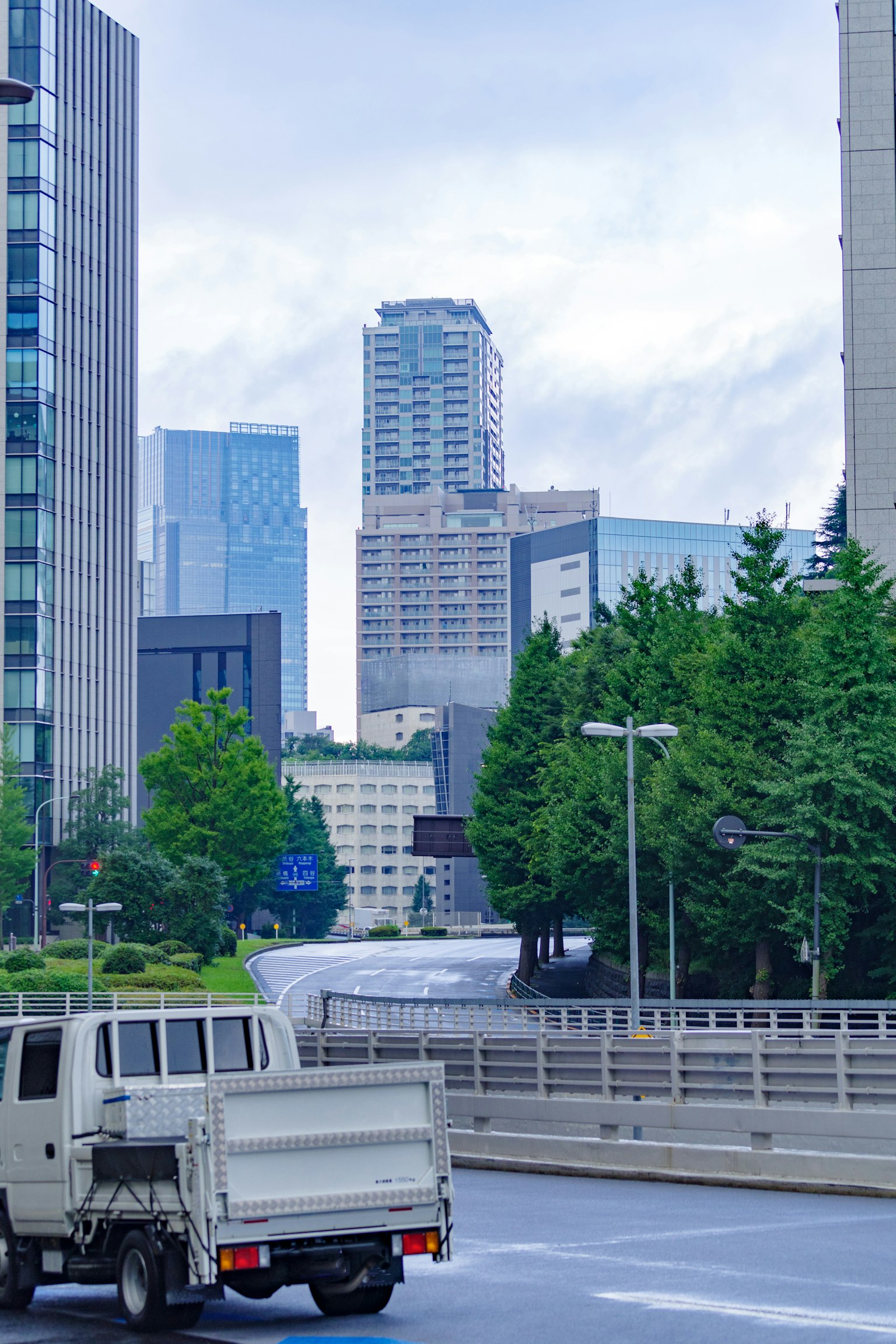 城市景观，摩天大楼与绿树相伴，路上有一辆卡车