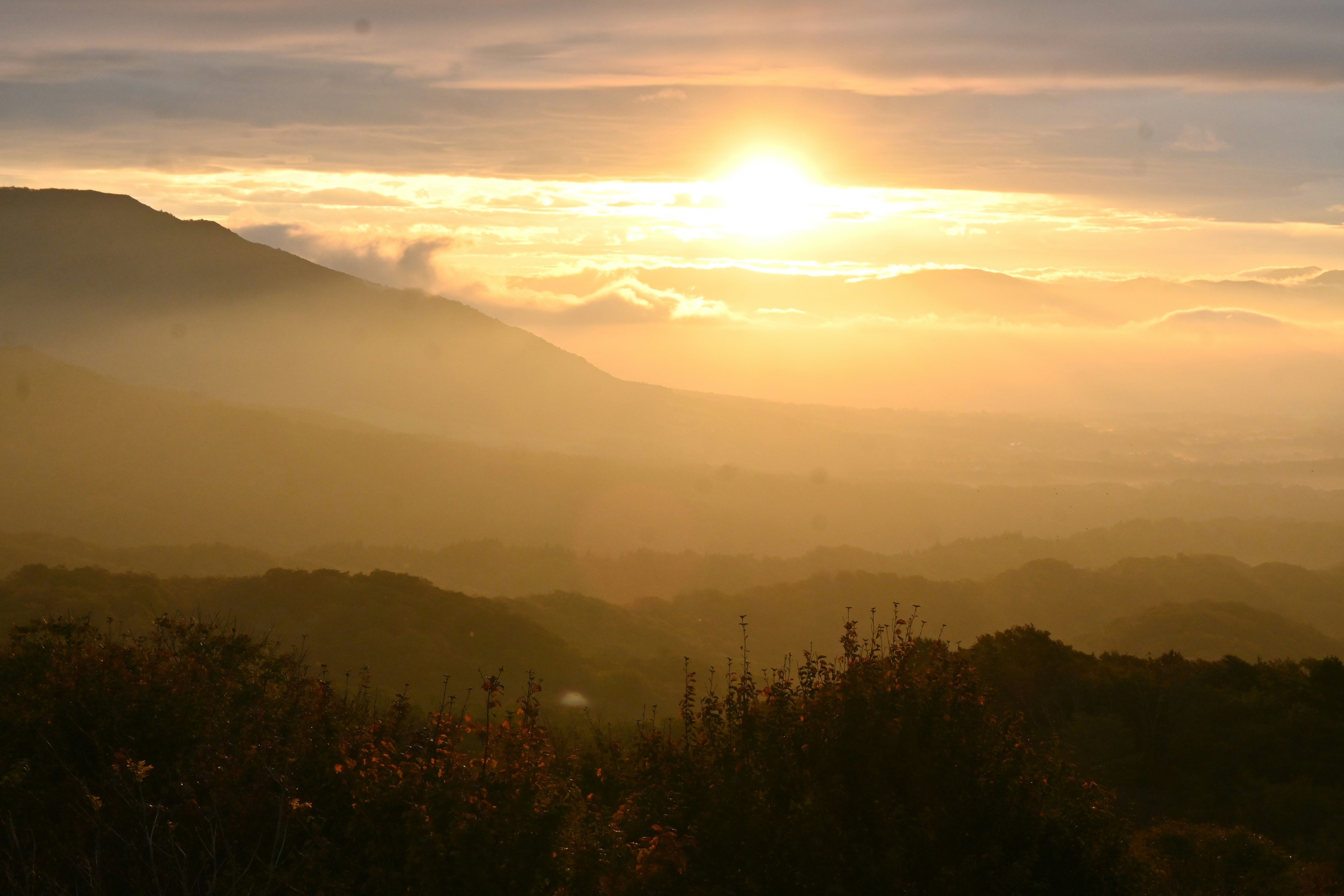 夕日に照らされた山並みと霧のかかった谷の風景