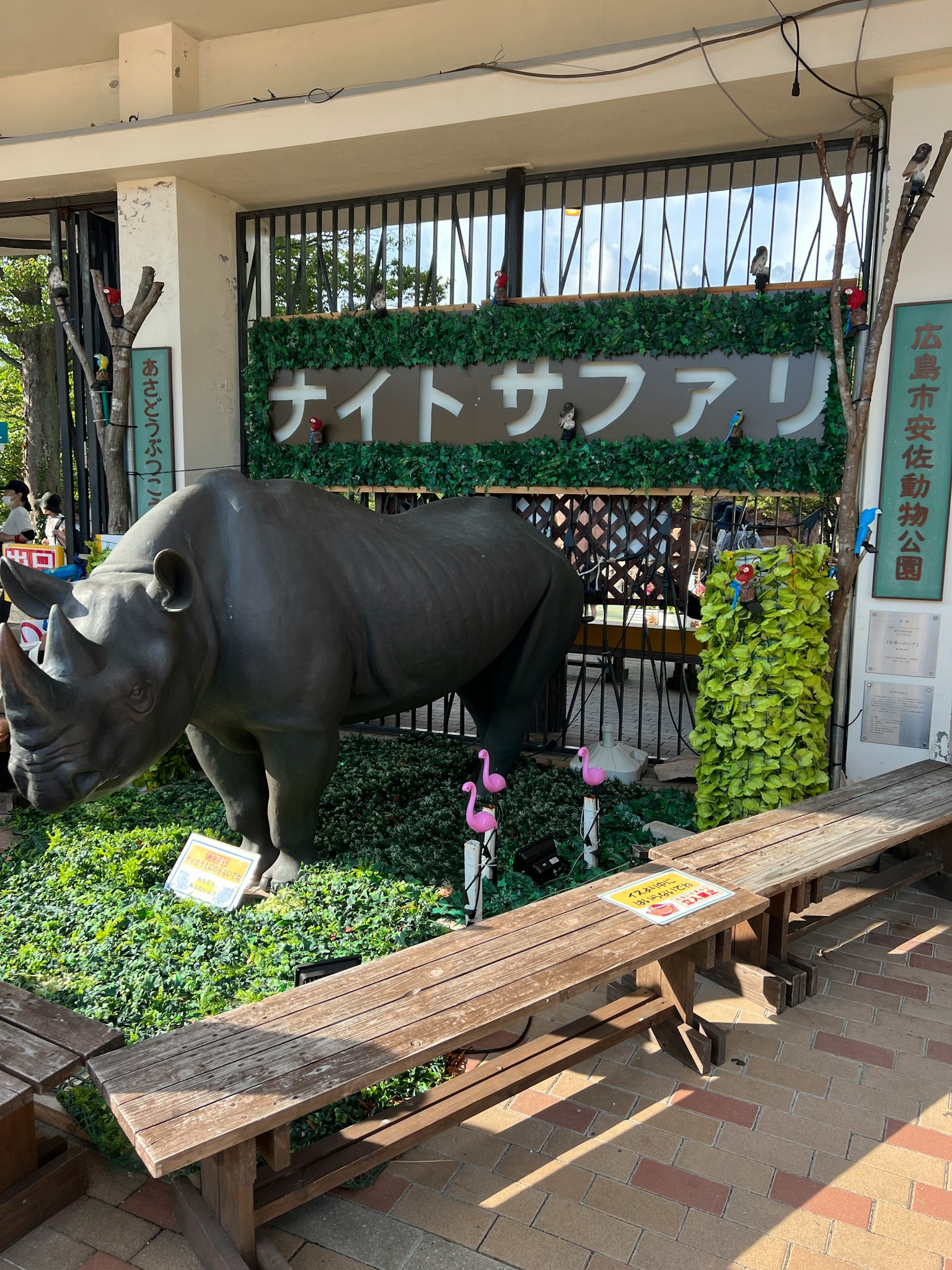 夜間野生動物園標誌前的黑犀牛雕像，周圍環繞著綠色植物
