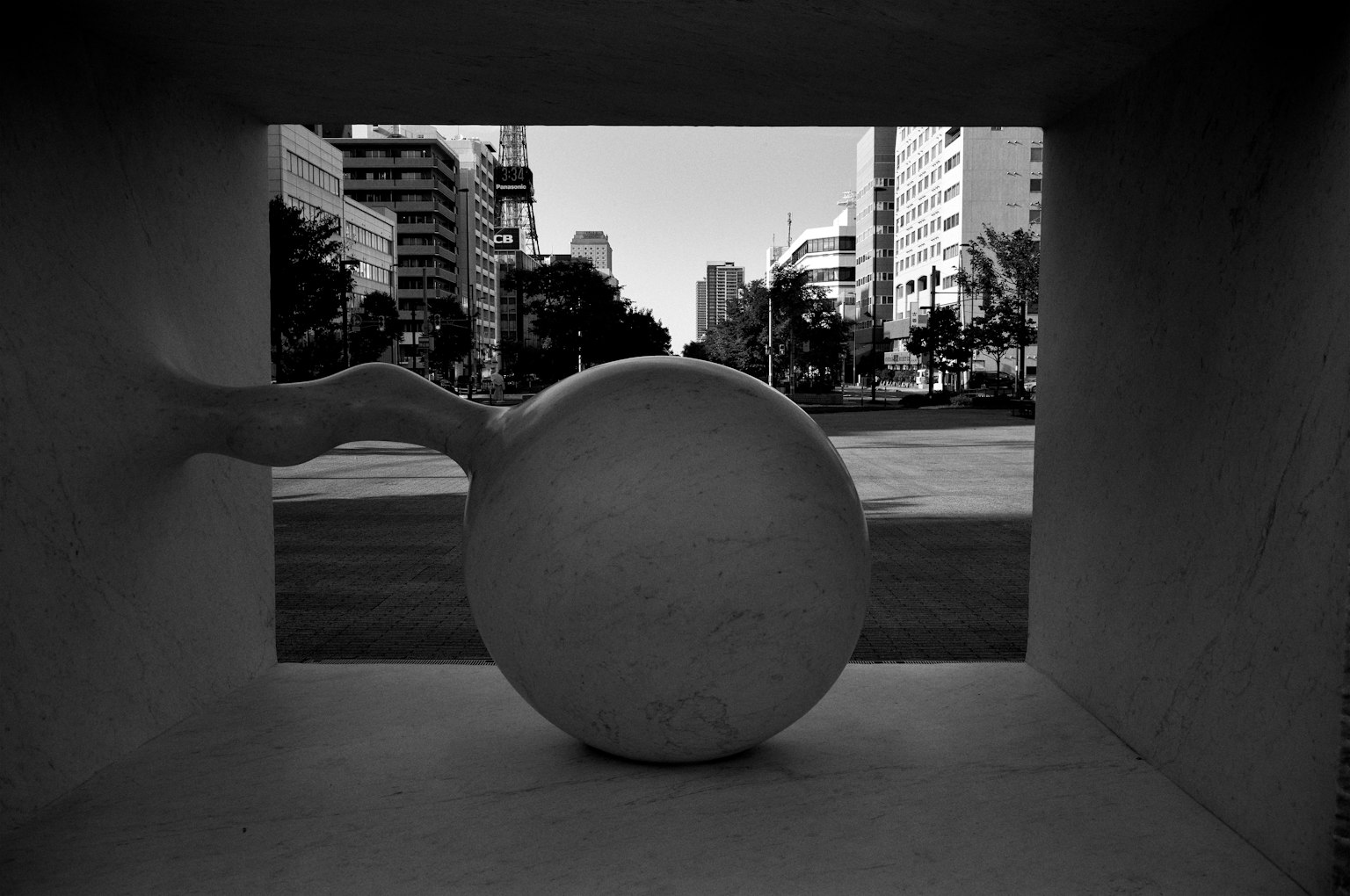 Escultura abstracta con forma esférica enmarcada por un paisaje urbano en blanco y negro