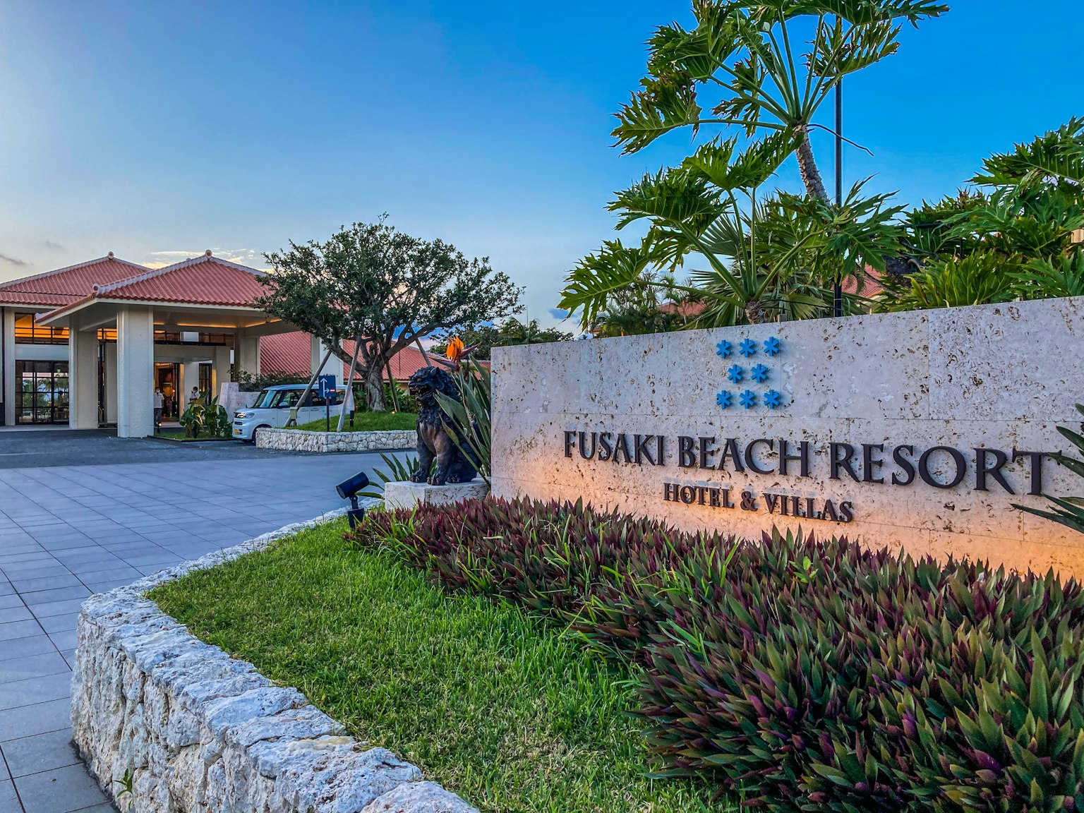 Pintu Fusaki Reach Resort dengan hotel dan vila dikelilingi oleh vegetasi subur dan langit biru