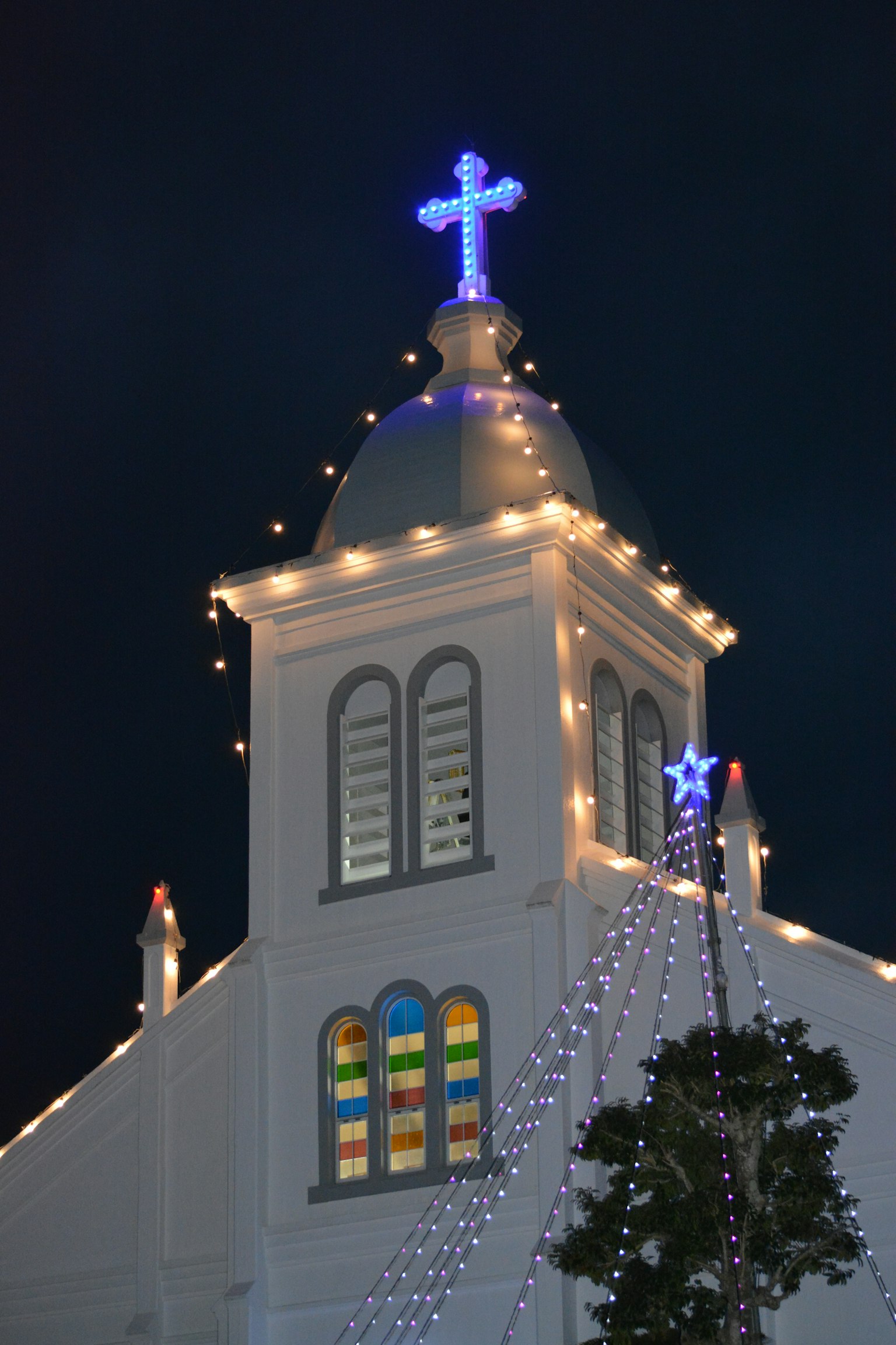 Church rooftop adorned with lights and a glowing cross at night