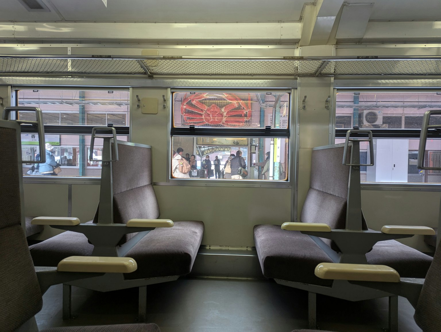 Interno di un treno con sedili e vista su persone fuori dalla finestra