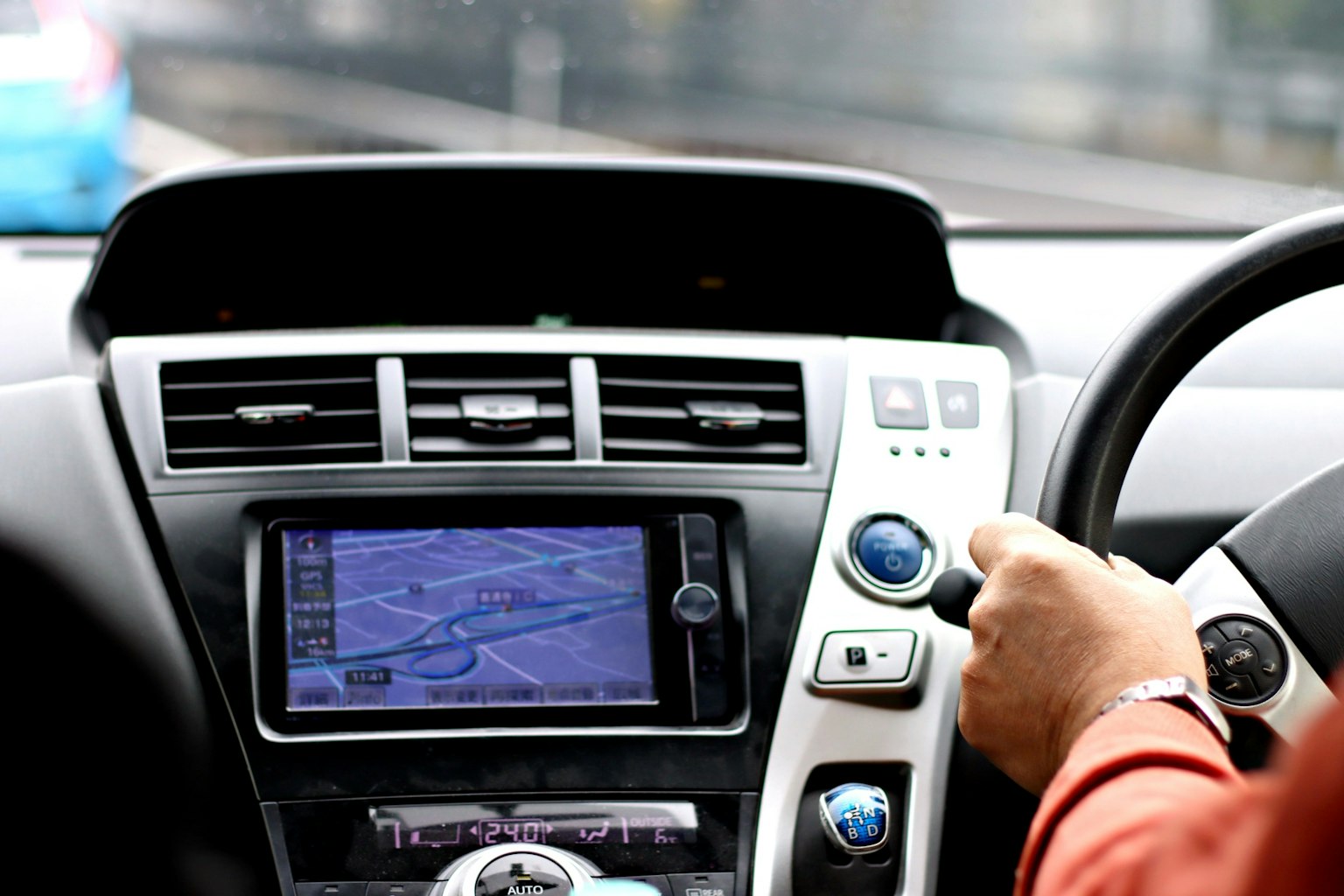 Interior de un coche mostrando una mano en el volante y un sistema de navegación