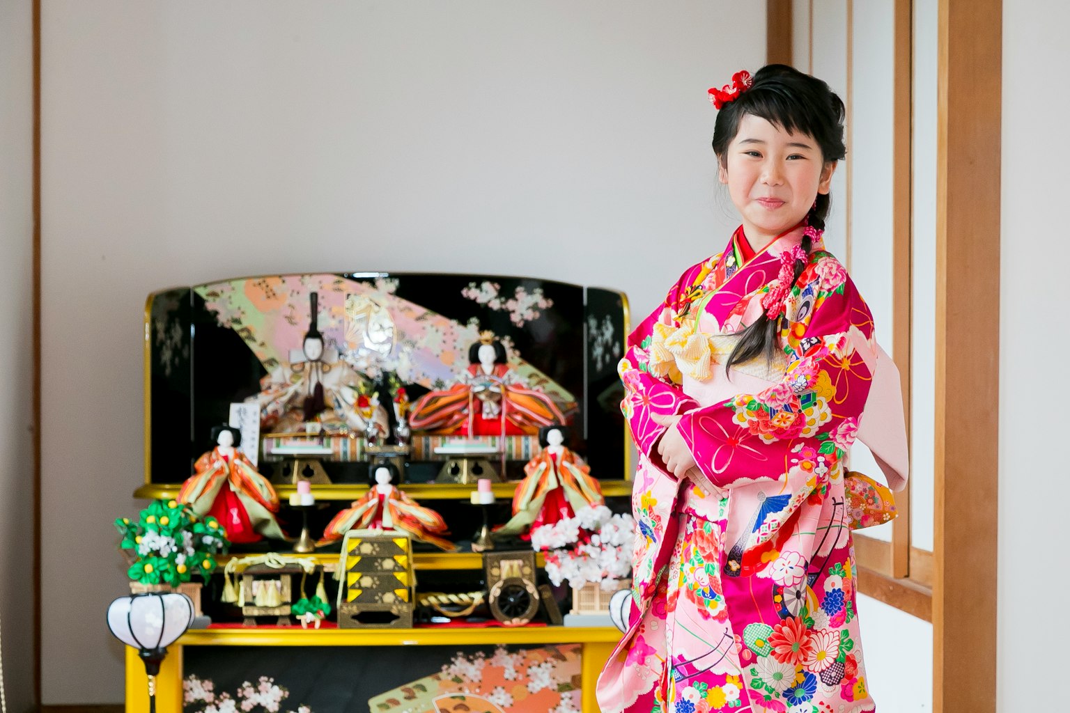 Ein Mädchen in einem bunten Kimono lächelt vor einer Hinamatsuri-Ausstellung