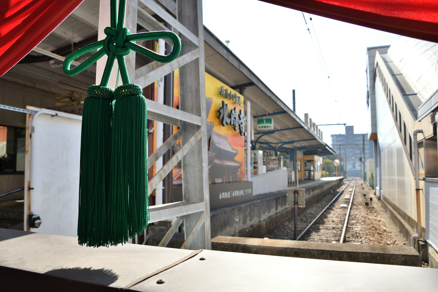 Vista di una piattaforma ferroviaria attraverso una finestra con frange decorative verdi in primo piano